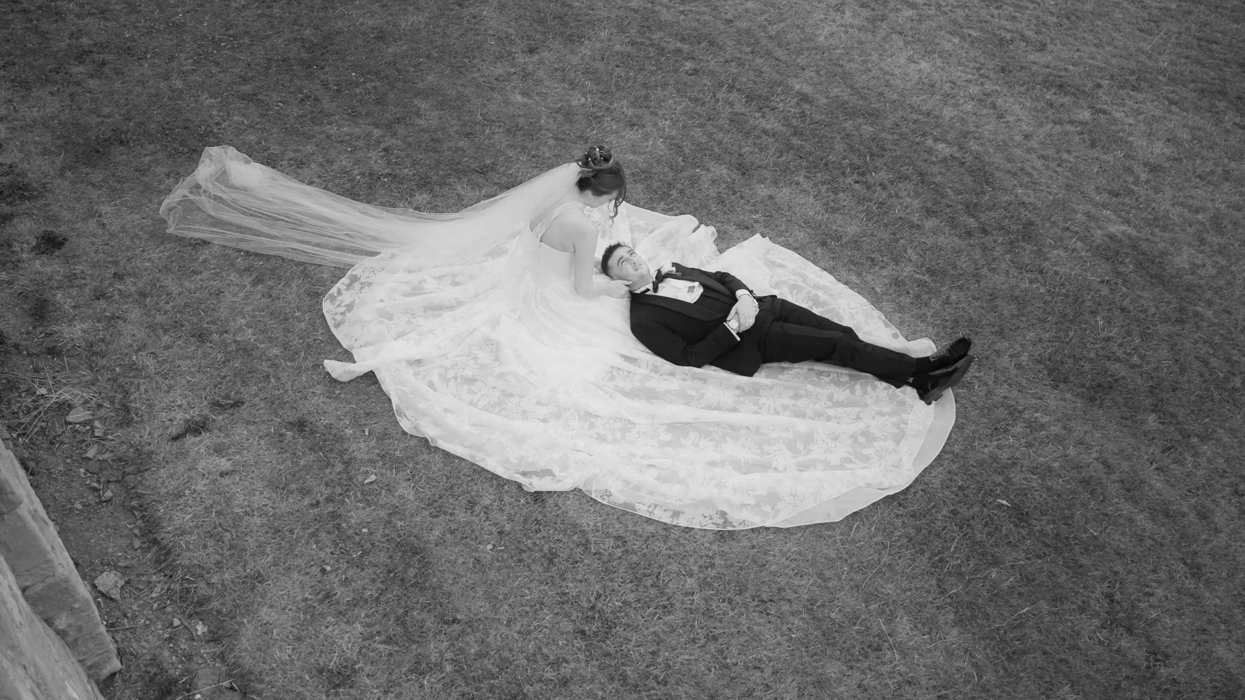 Groom looking lovingly into his brides eyes whilst laid backwards on the brides stunning wedding dress