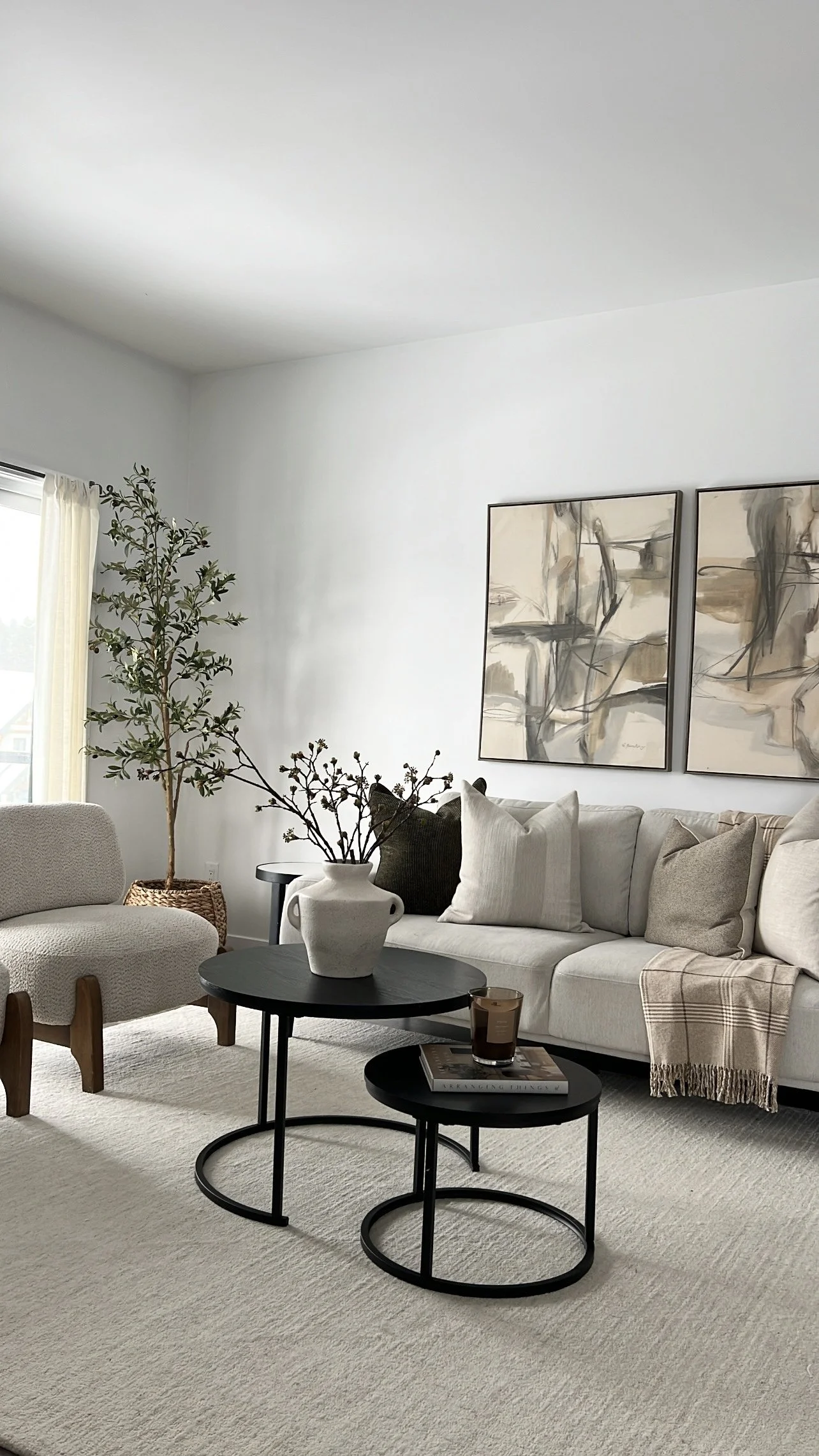 Living room with a cream sofa, black coffee tables, a potted plant, and abstract wall art.