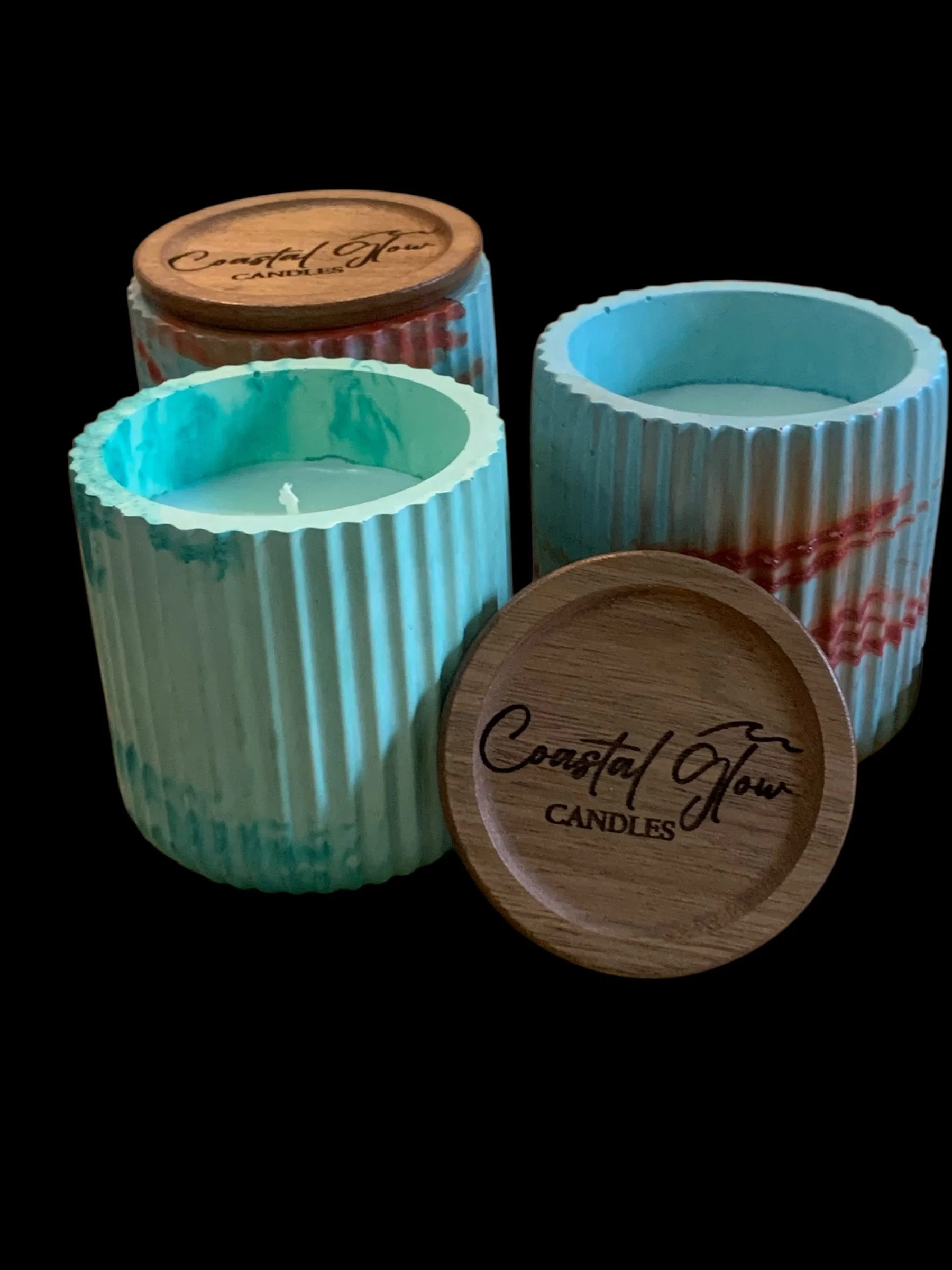Two turquoise ribbed candles and two wooden lids with 'Coastal Flavour Candles' engraved on them, on a black background.
