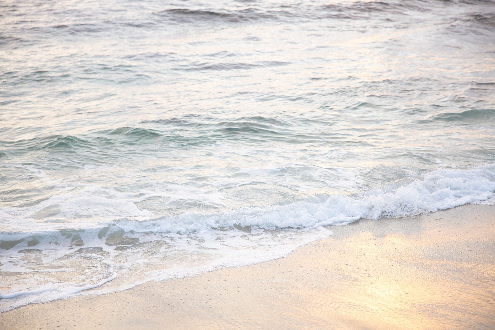 Calm ocean waves gently washing onto a sandy beach during sunset or sunrise.