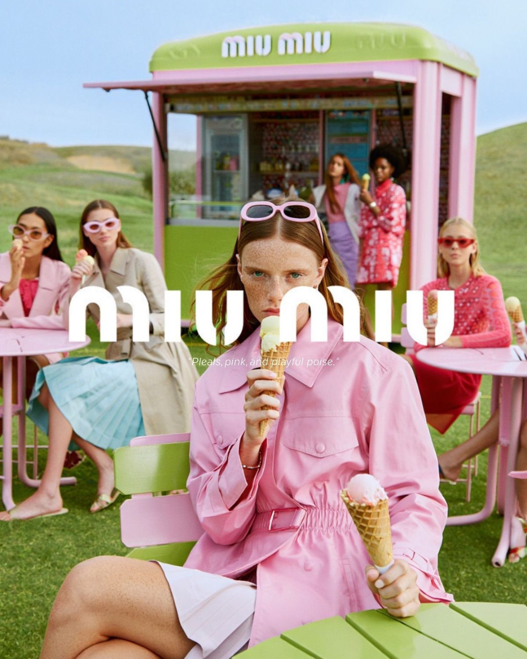Group of women with ice cream at an outdoor pink and green ice cream stand, with one woman in pink in the foreground holding a cone and sitting at a pink and green table.