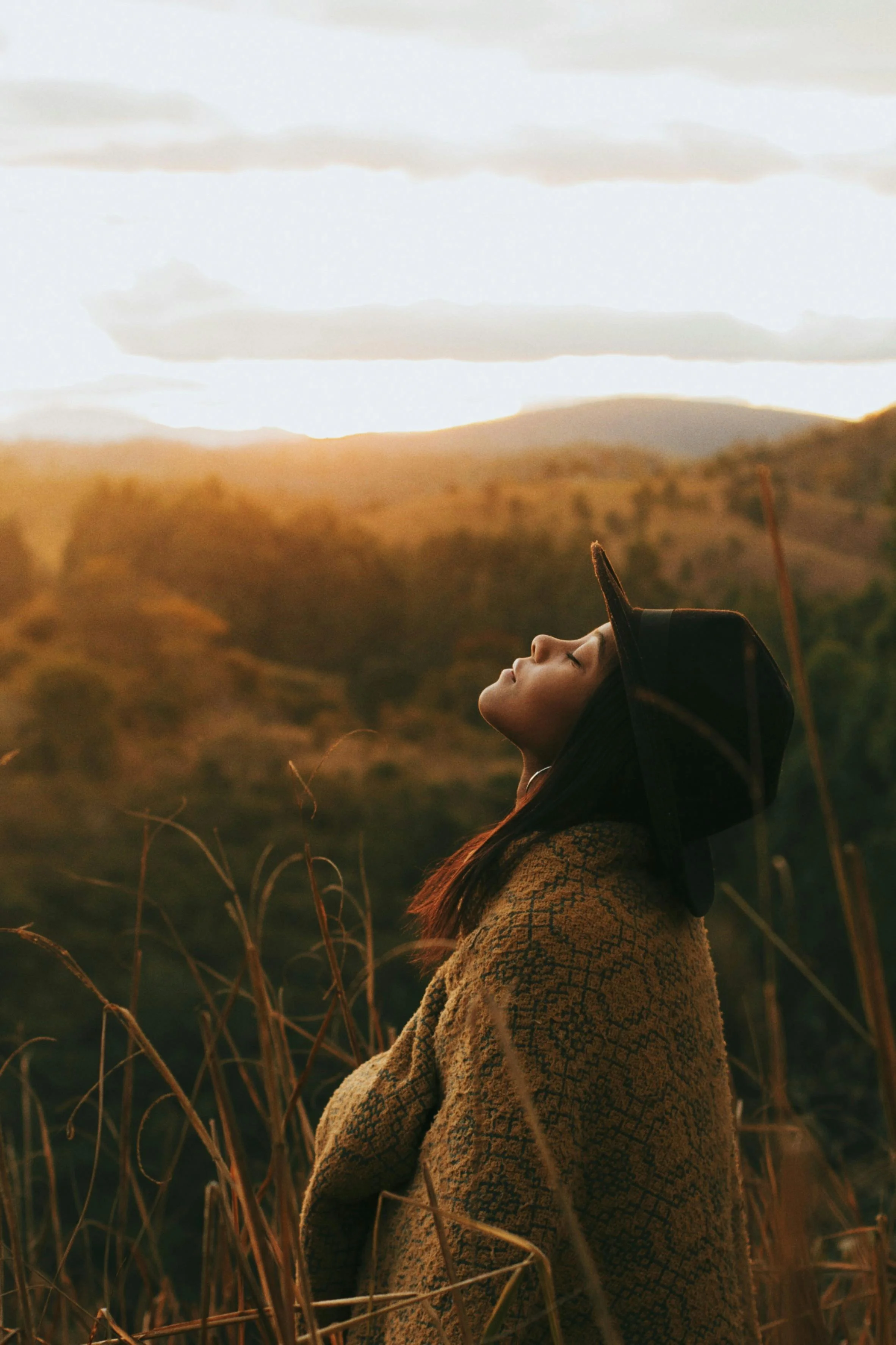 Wholistic chiropractic care offered represented by a woman practicing yoga outdoors at sunset, standing on grass with arms extended behind her and head tilted back slightly.