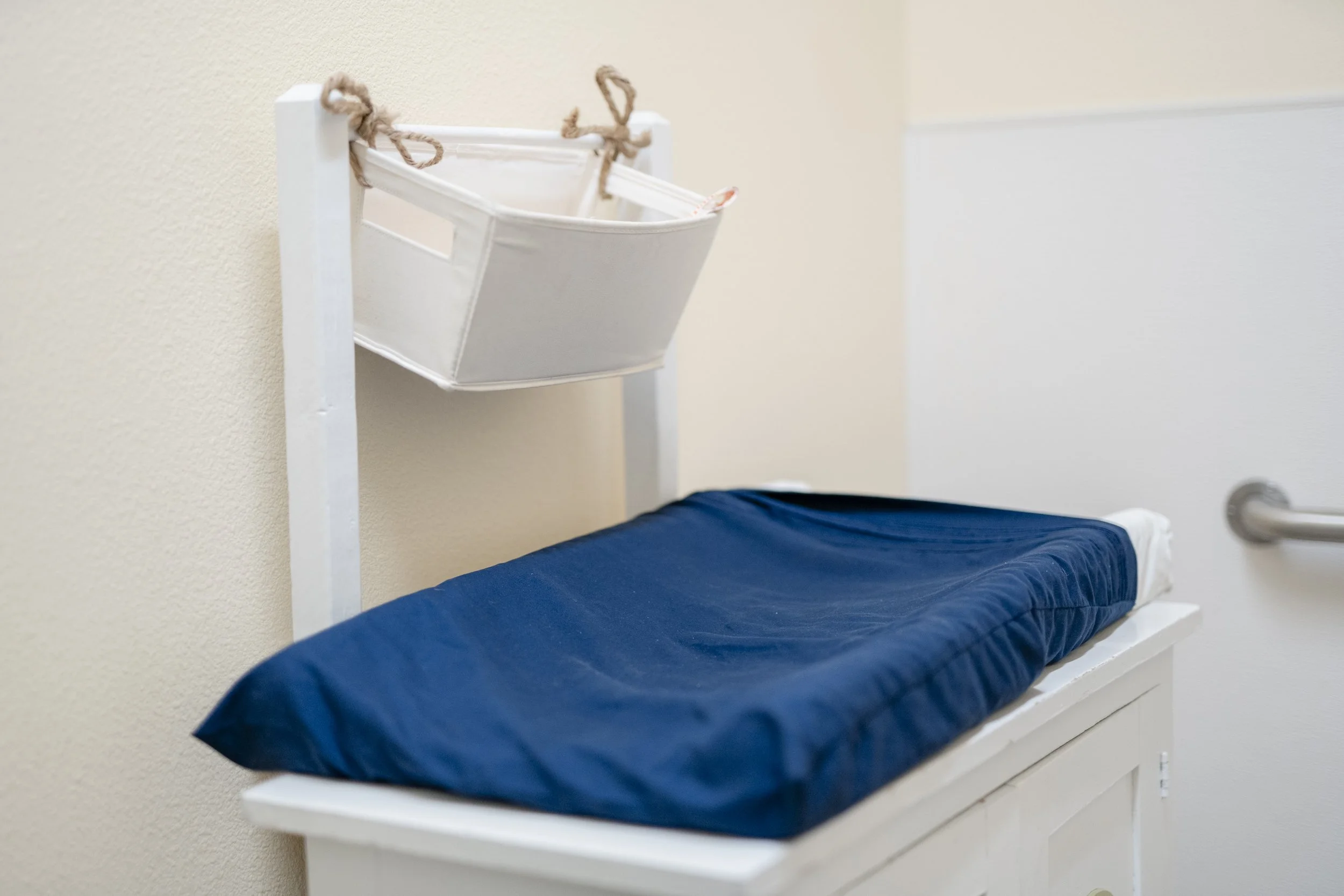 Hospital changing table with a padded blue surface and a white storage basket attached to the frame.
