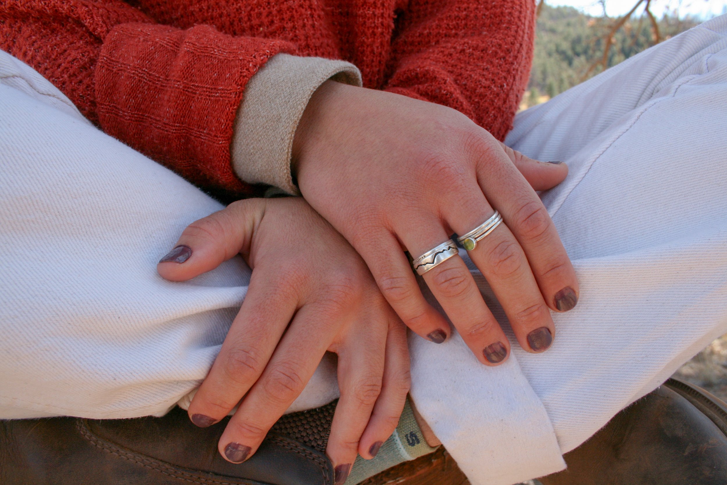 Close-up of two hands with rings resting on each other, one hand on top of the other, with a scenic outdoor background.