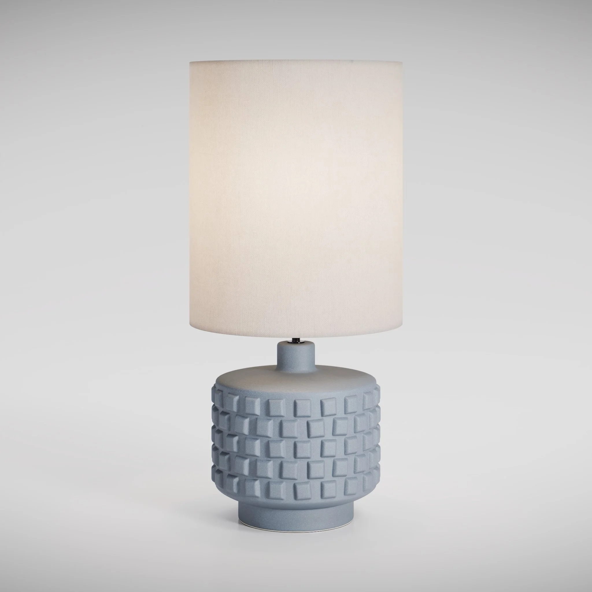view of a modern type of table lamp, with a fabric shade, with a warm light on in a white studio