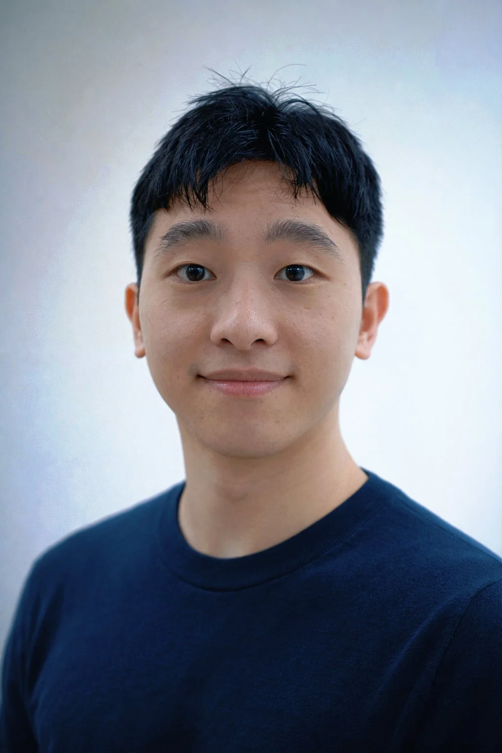 Portrait of a young Asian man with short black hair, wearing a black T-shirt, smiling slightly, against a plain light background.