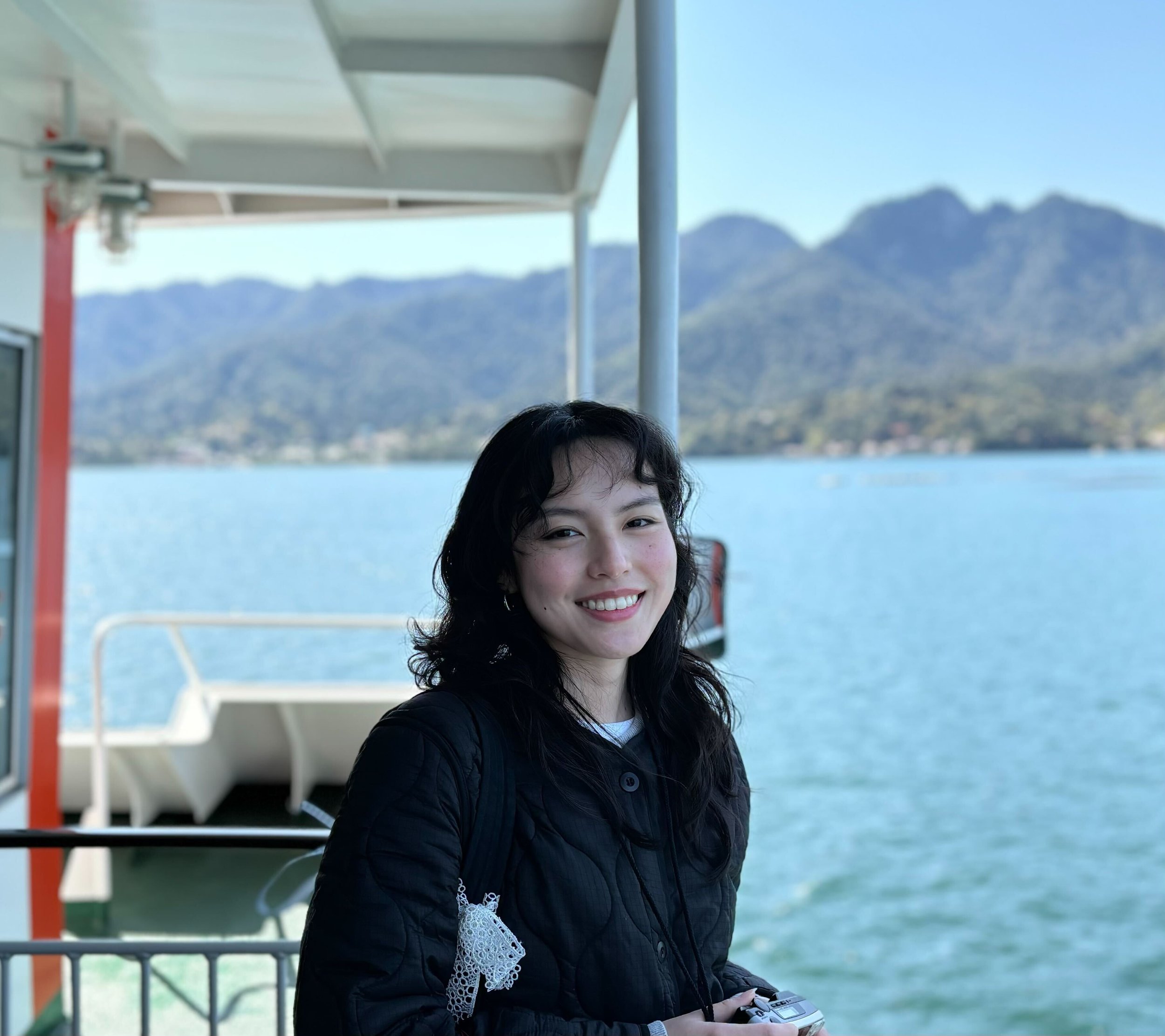 Miu standing in front of water and mountains.