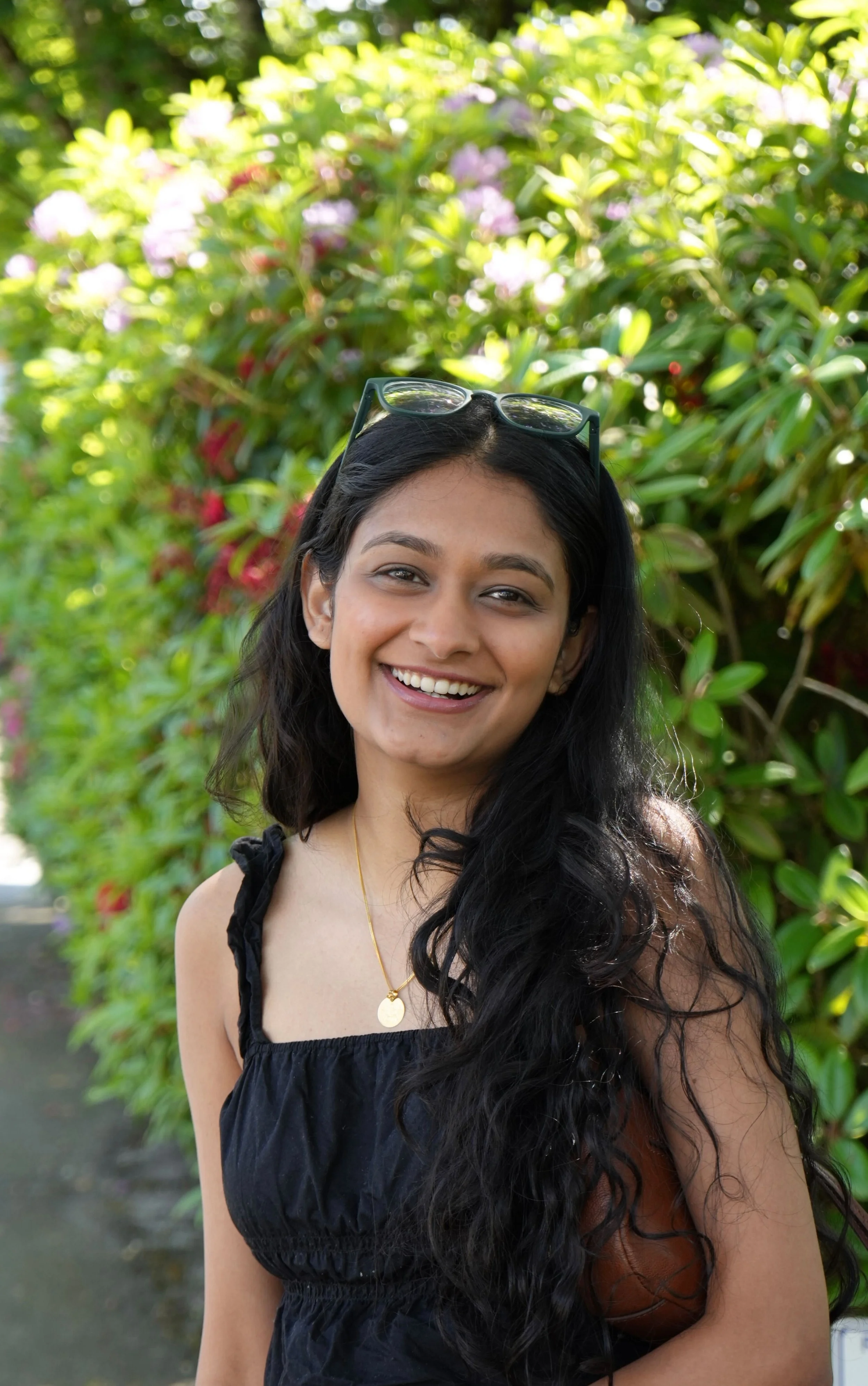 Riya standing in front of a vibrant green hedge while smiling at the camera