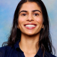 Rajdeep smiling. Blue background- headshot.