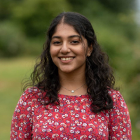 Zainab smiling in park. Green trees and shrubs in background