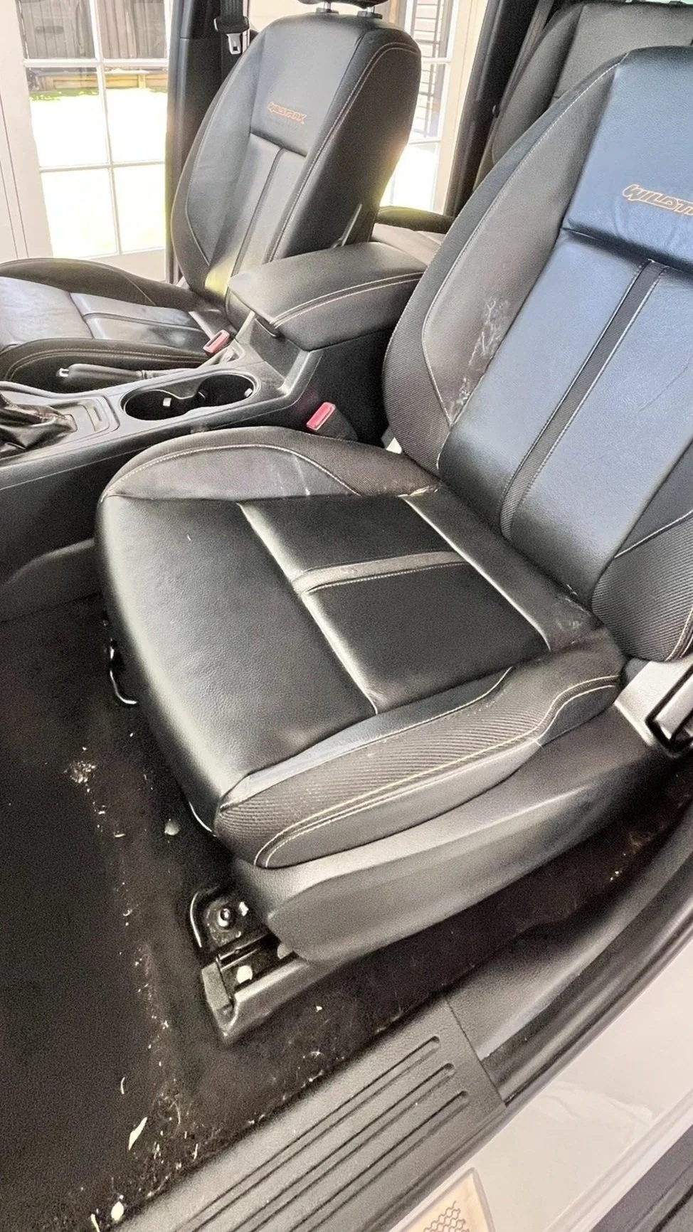 Close-up of the black leather front seat and part of the back seat in a vehicle, showing some dirt and wear.