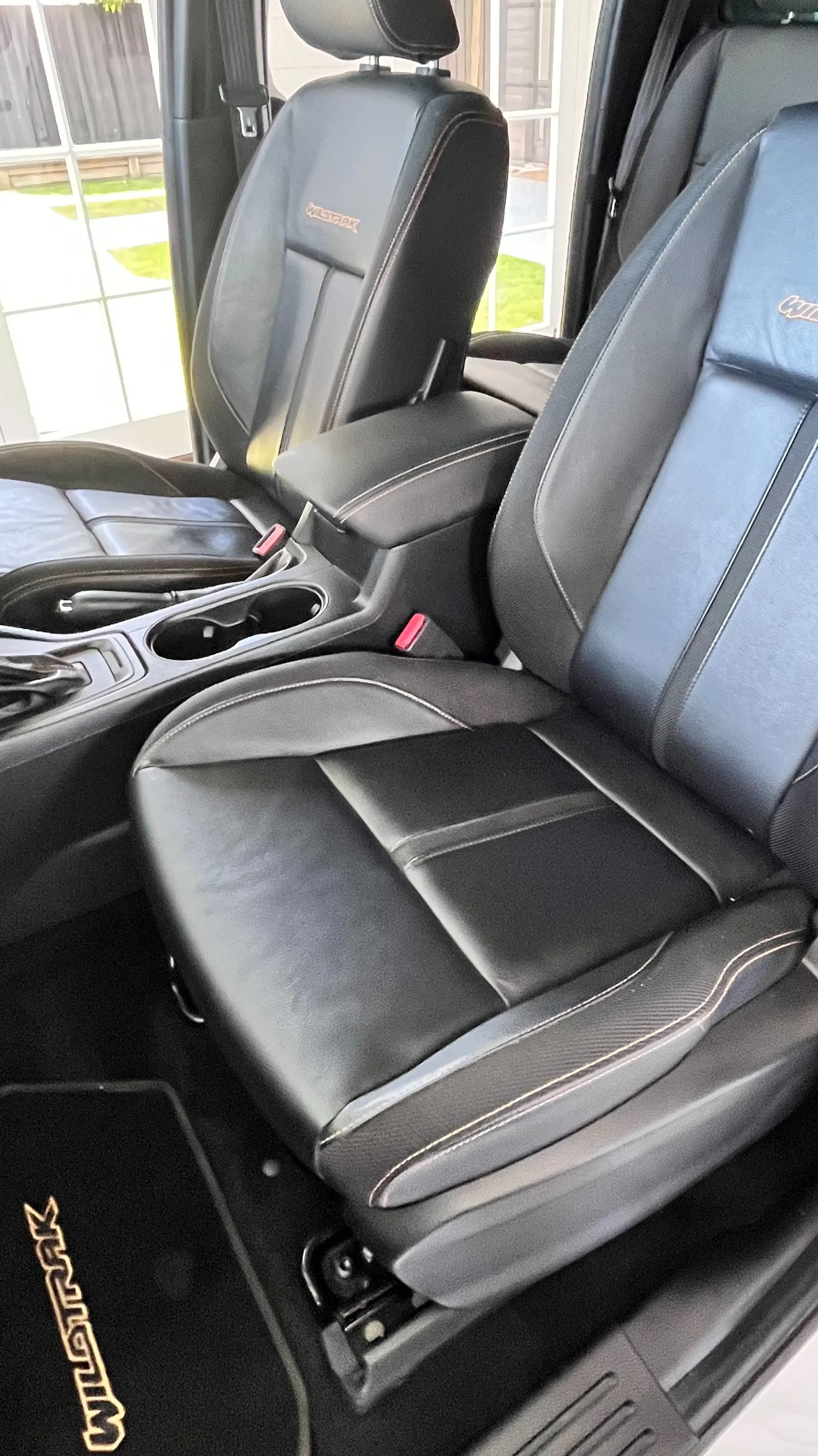 Front seats of a black Jeep with leather upholstery, showing the center console, cup holders, and Jeep logo on the headrests.