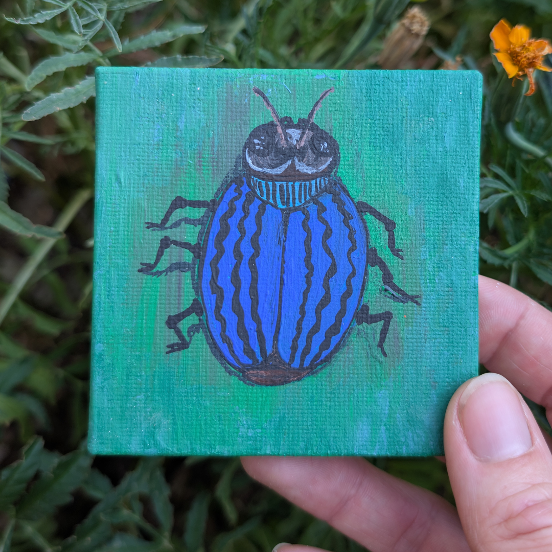 A small painting of a blue and black striped beetle on a green background, held by a person's hand amidst green foliage and a small orange flower.
