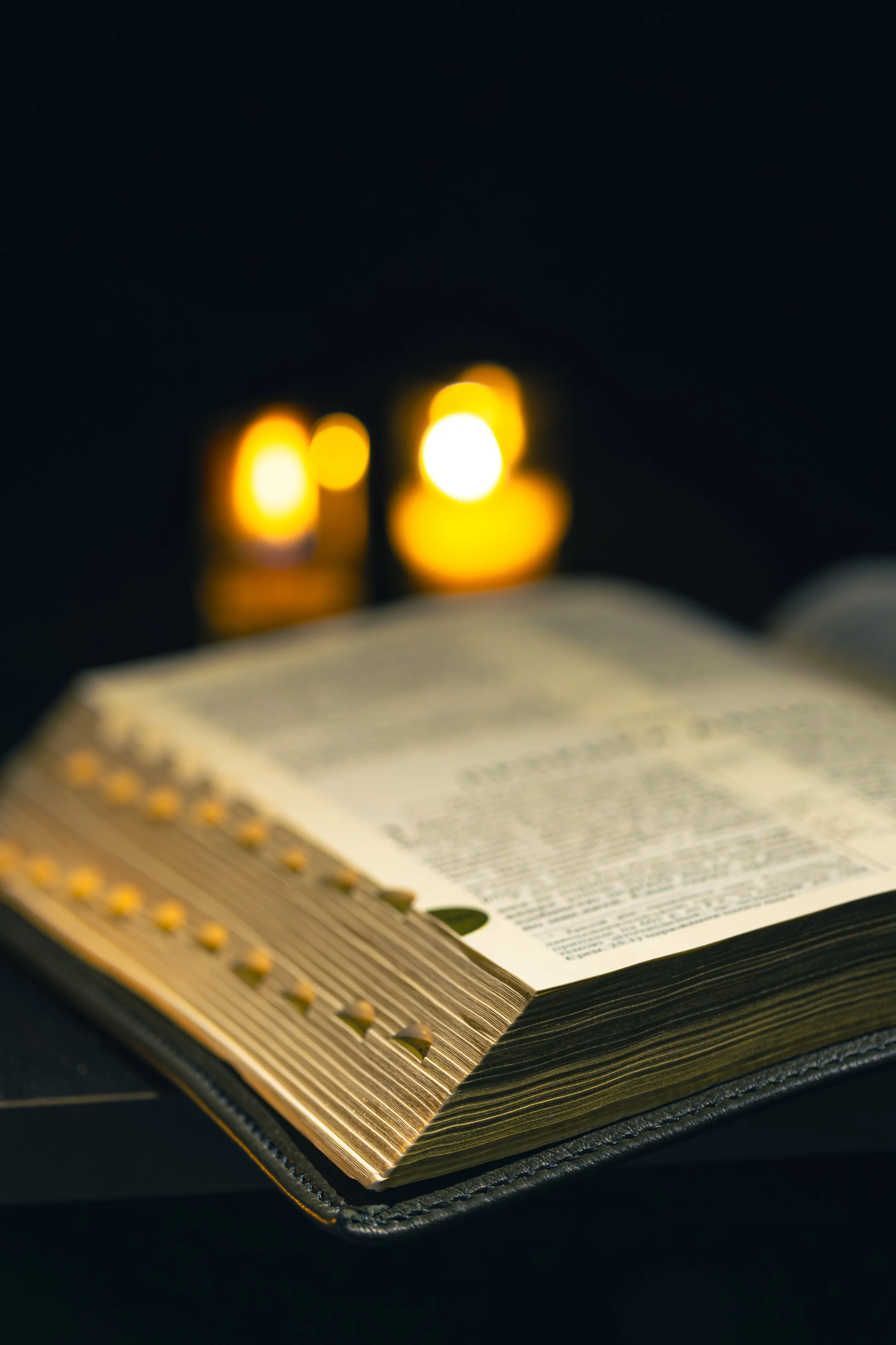 Open Bible on a black leather cover with candles in the background.
