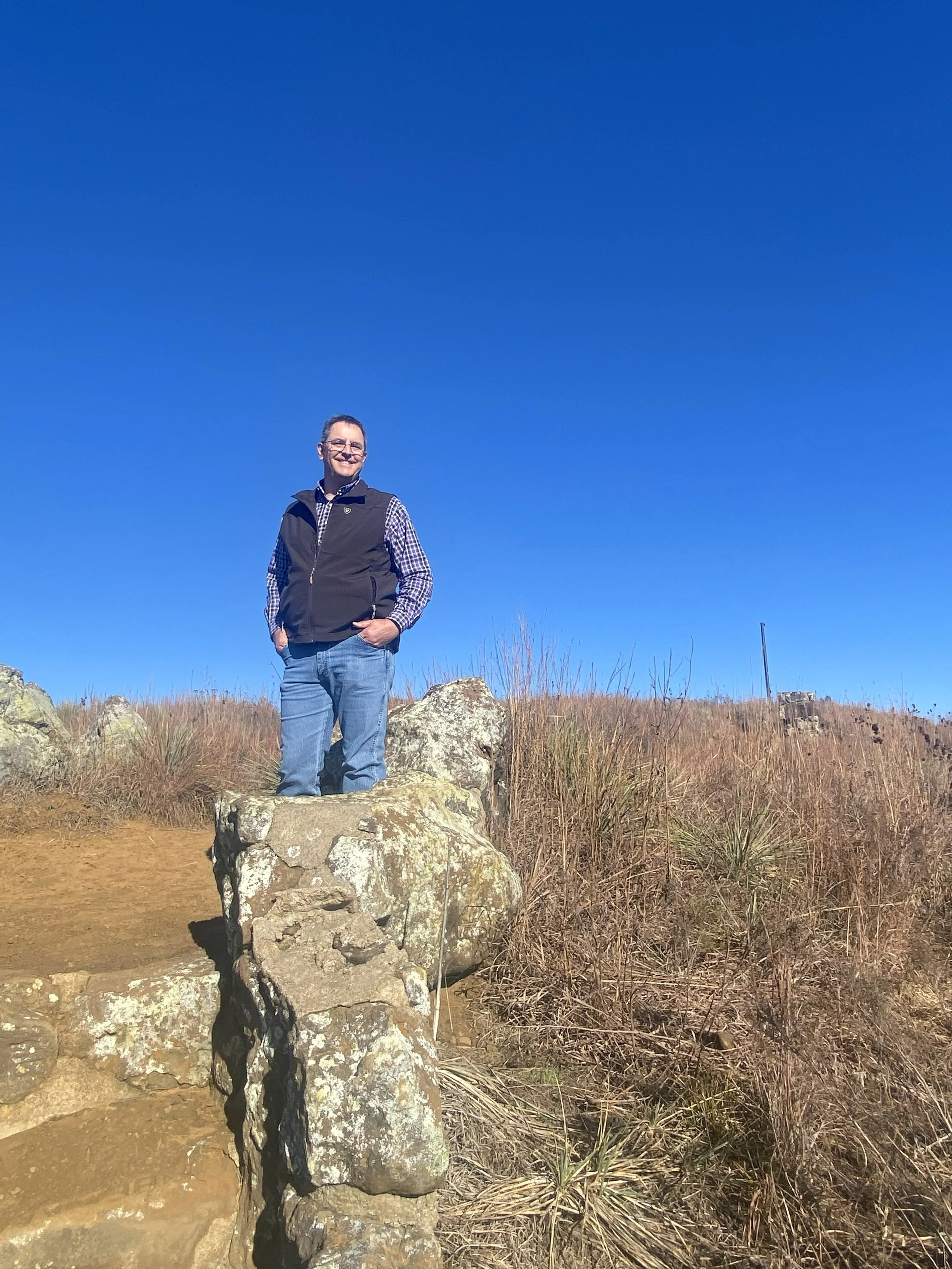 Family of four standing in a grassy field, smiling at sunset, wearing casual outfits.