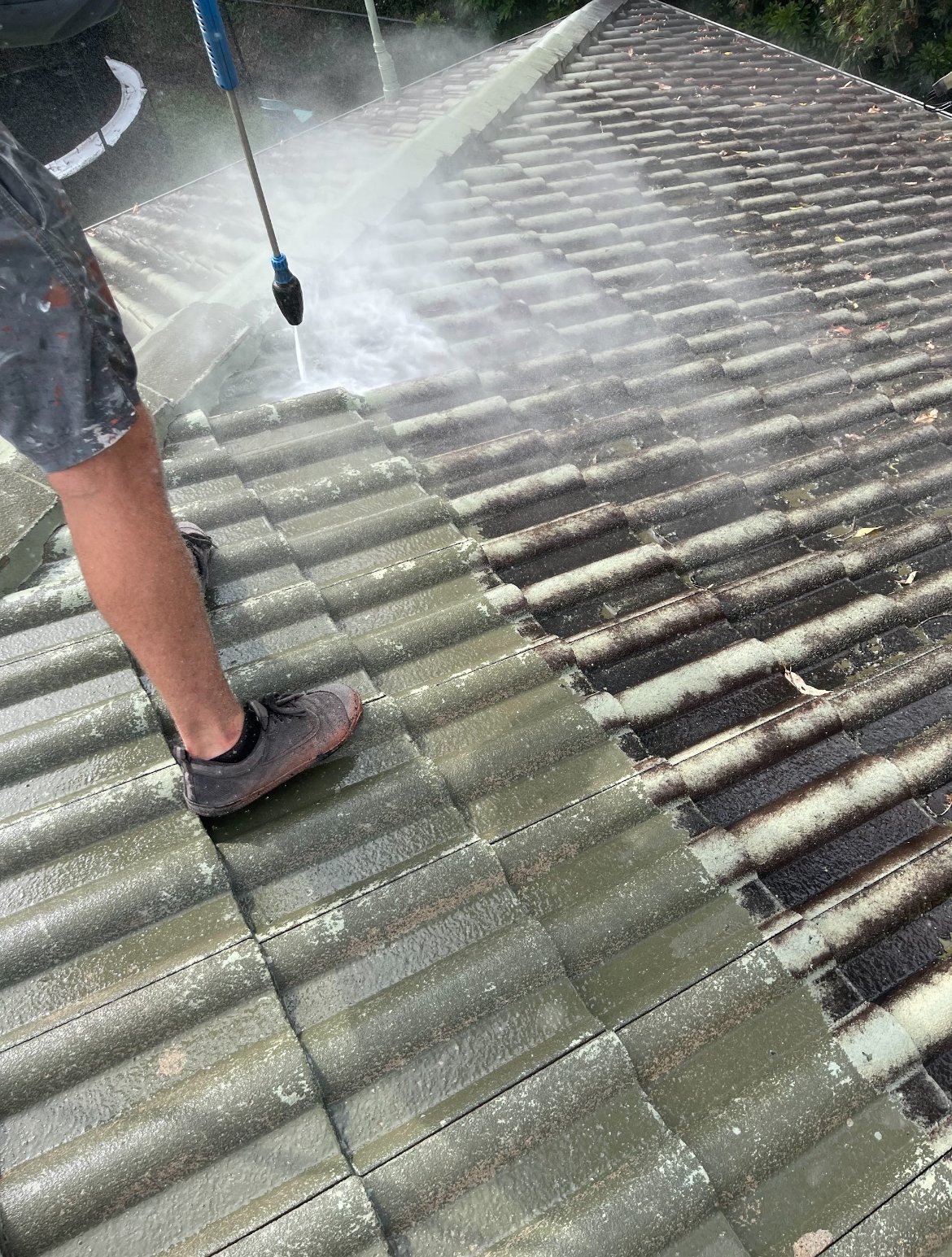 Person pressure washing a tiled roof to remove dirt and algae.