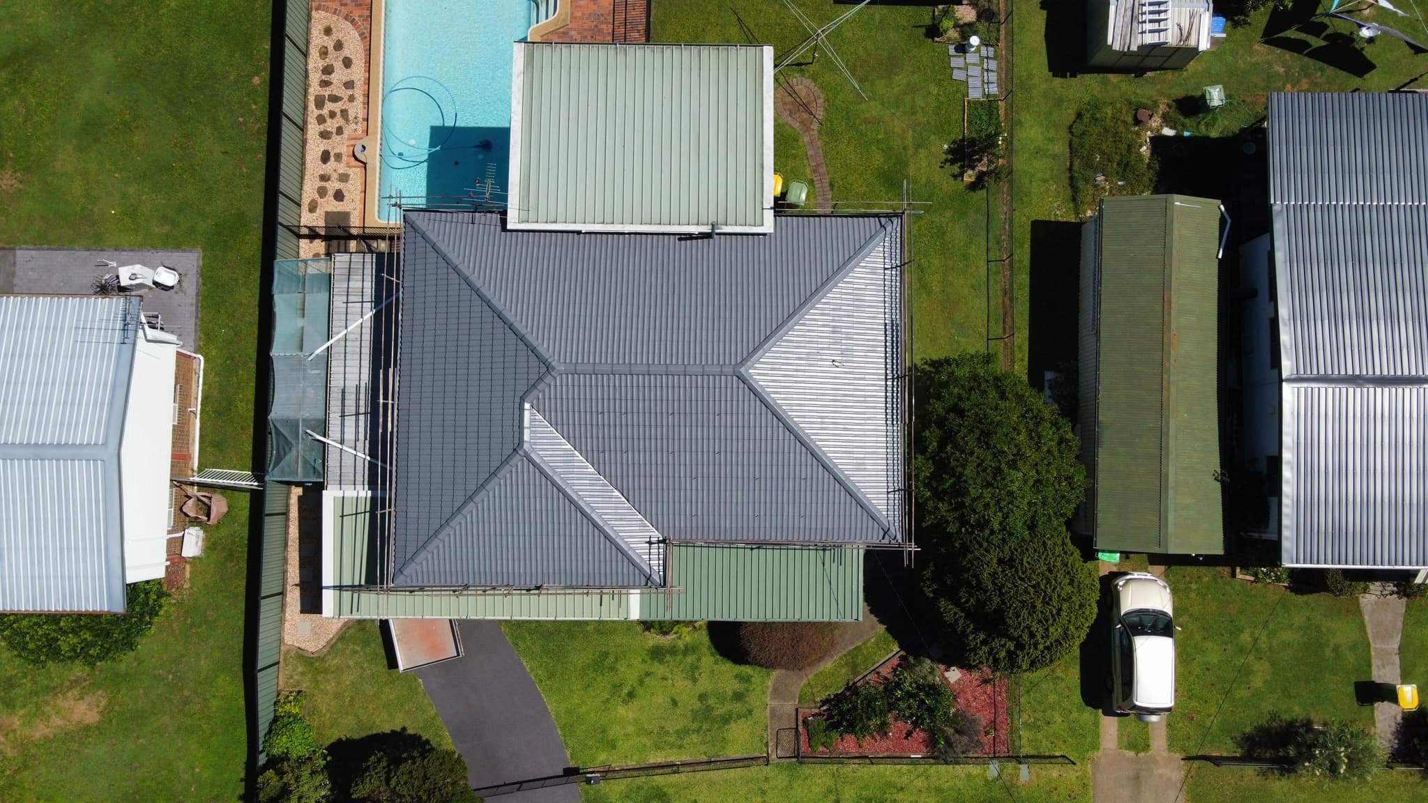 Aerial view of a residential backyard with a house, a swimming pool, and a garden with trees and grass.