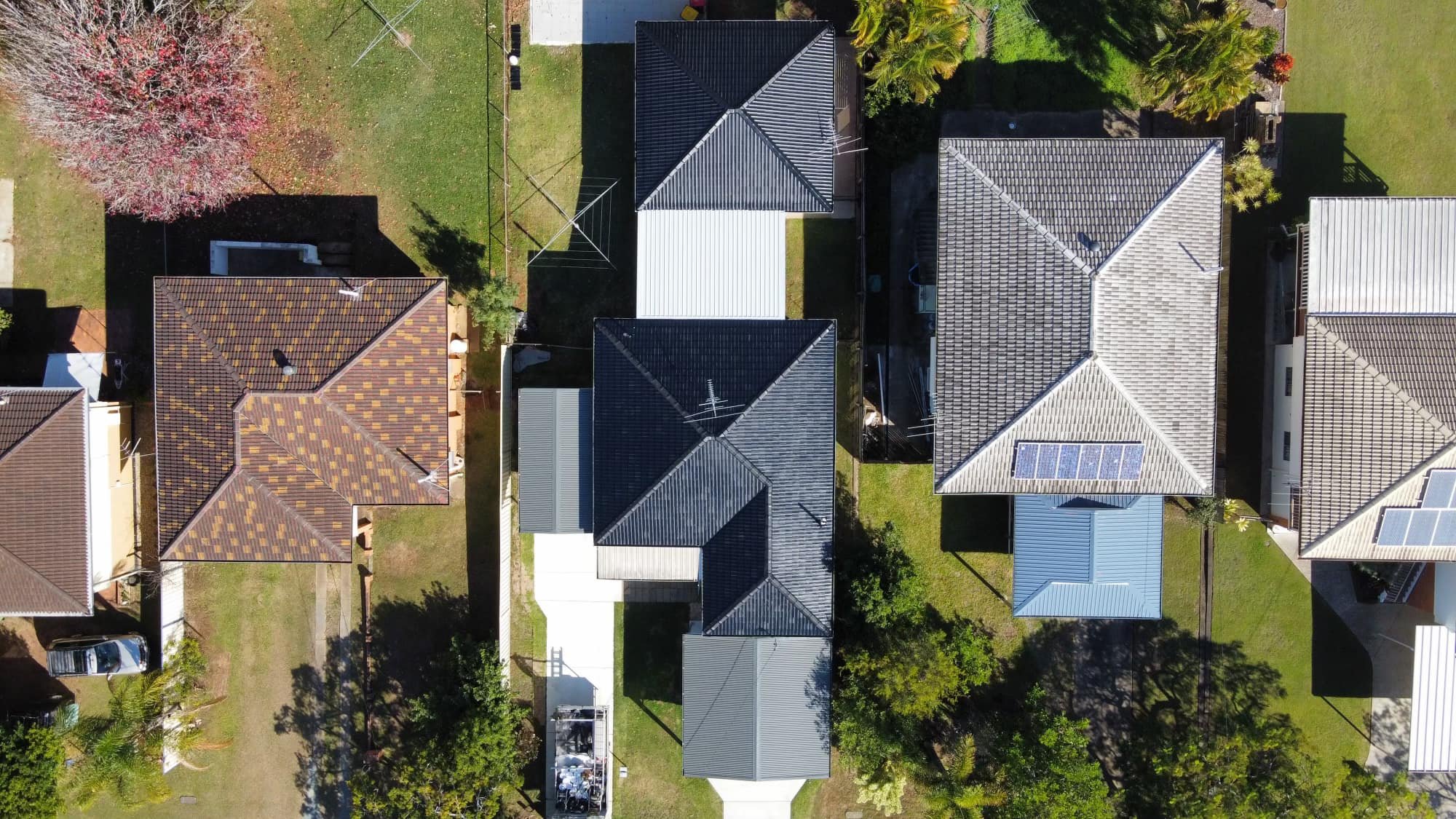 Aerial view of several houses with different roof styles and colors, surrounded by green lawns and trees.