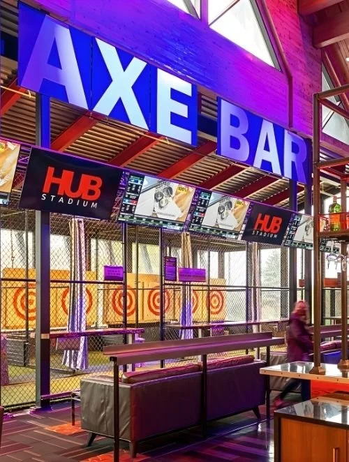 Inside an AXE Bar at HUB Stadium with electronic screens, seating areas, and target shooting stations.