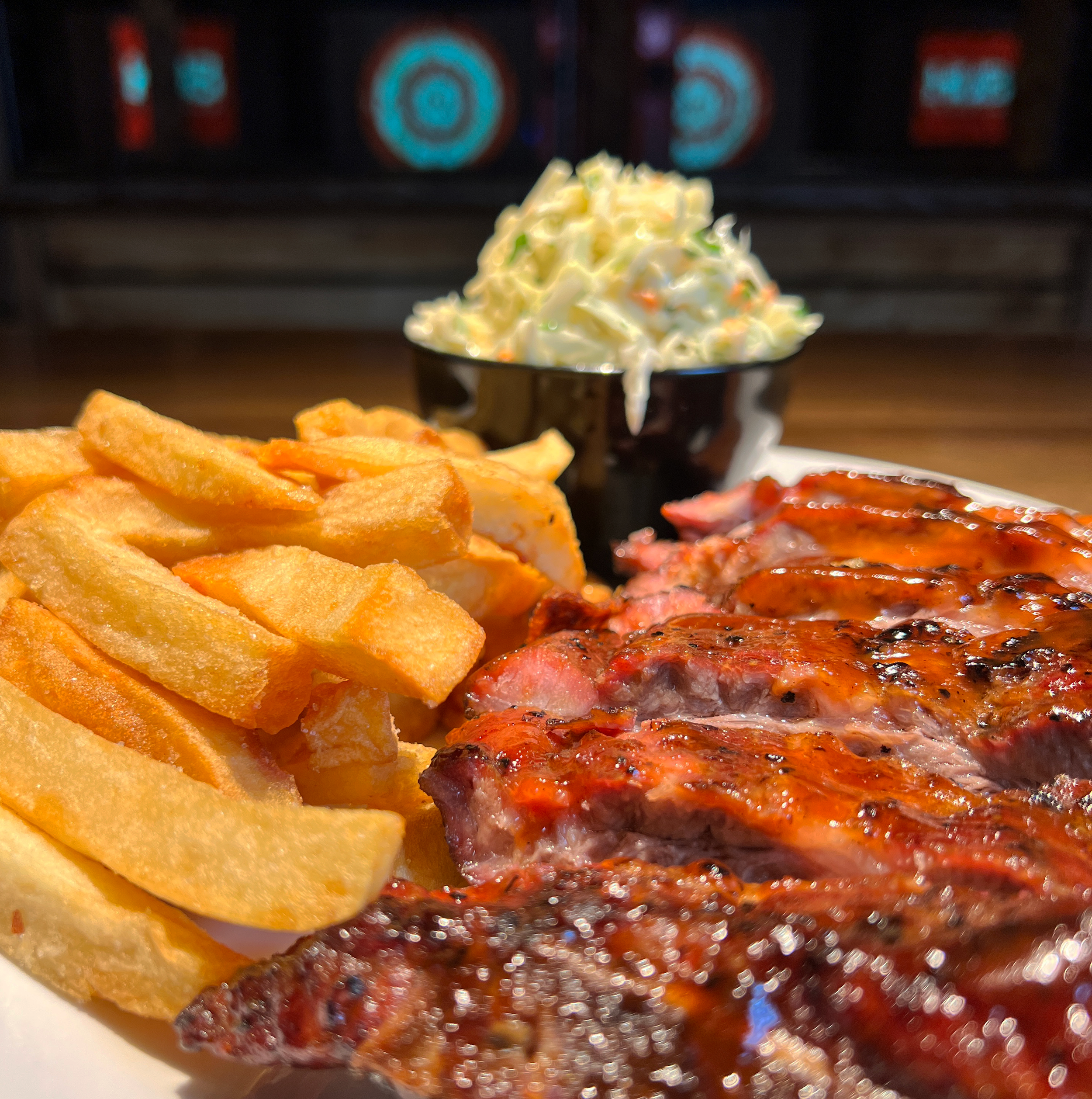 Close-up of a plate with French fries, barbecue ribs, and a side of coleslaw in a black cup.