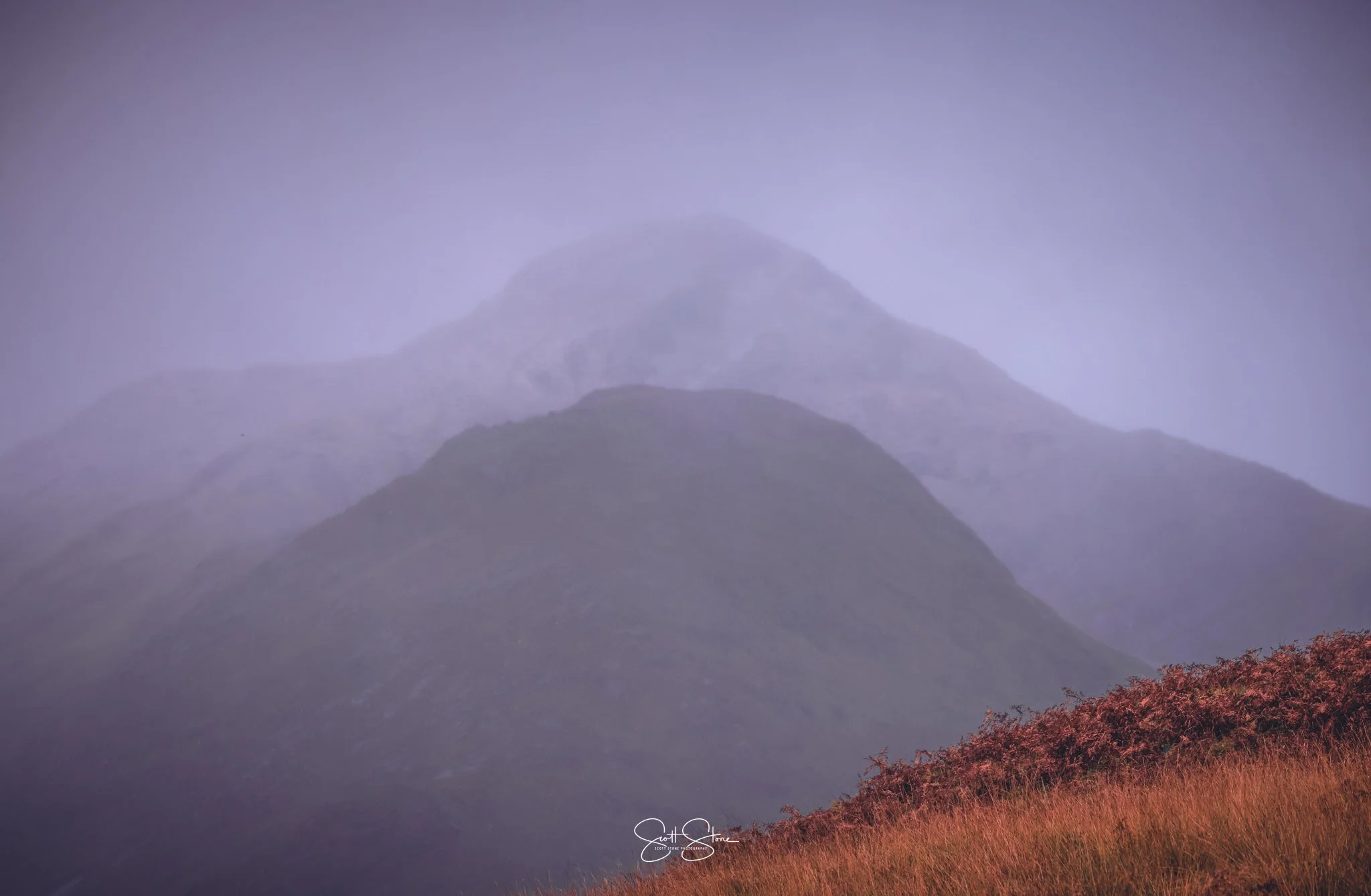 Multiple mountain peaks with mist or fog, with orange and red foliage at the foreground.