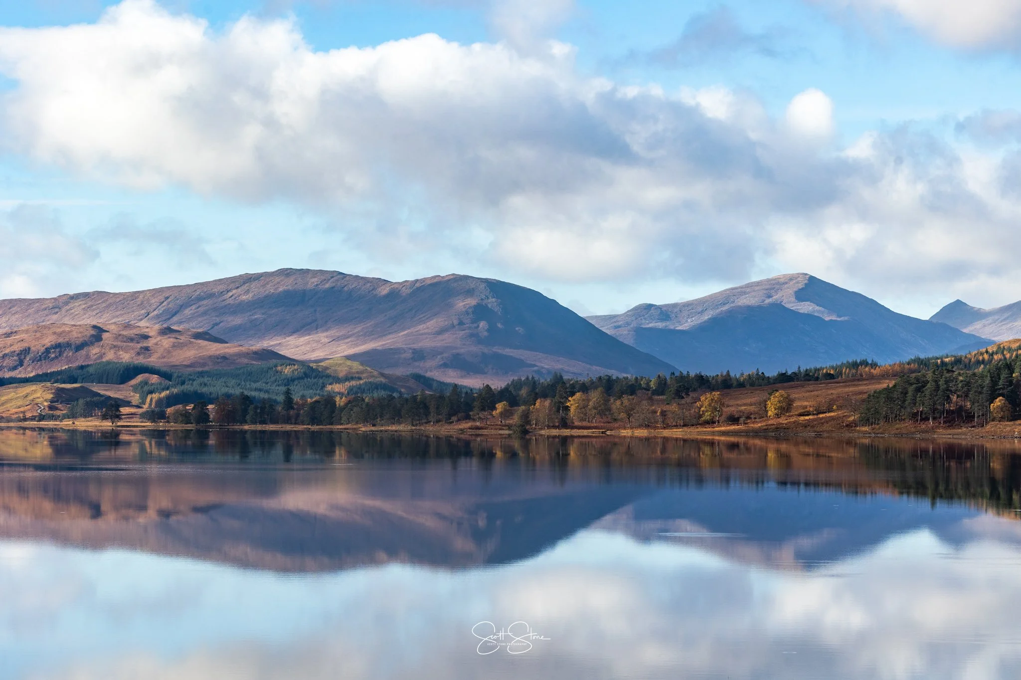 Scenic landscape of mountains reflected in a calm lake with partly cloudy sky.