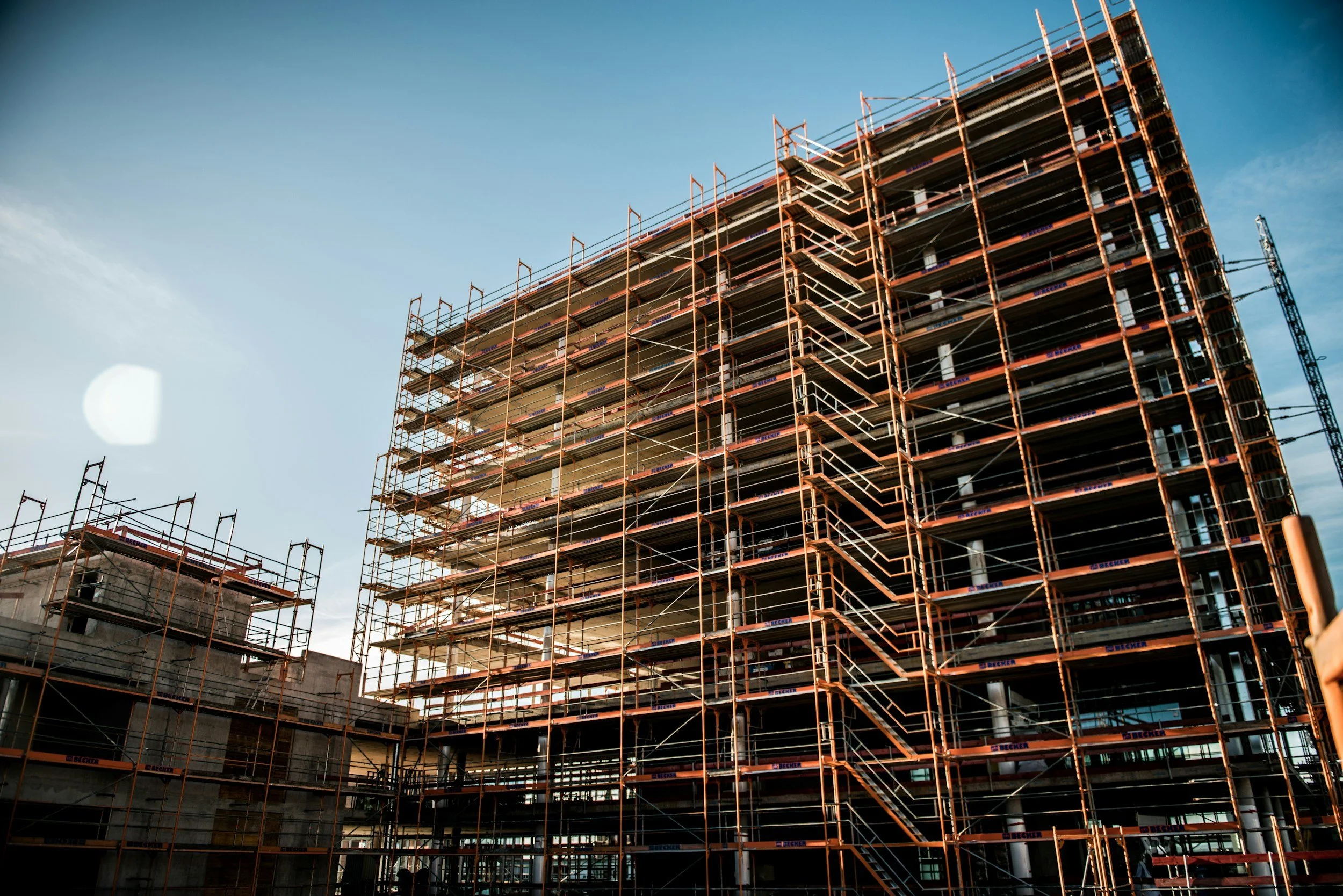 A multi-story building under construction with orange scaffolding, against a blue sky.