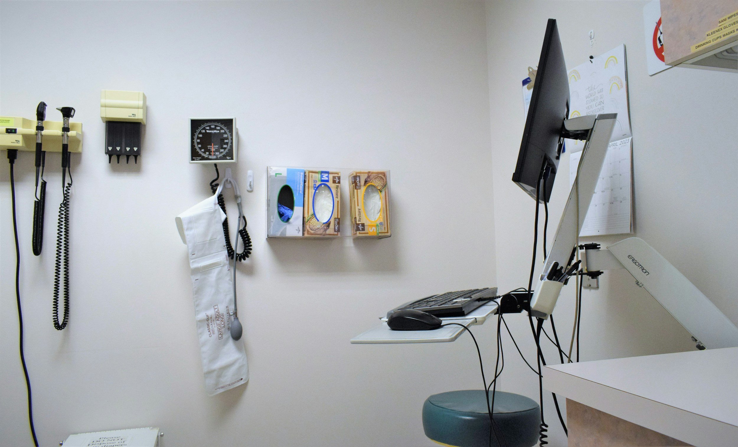 Wall of doctors office with boxes of gloves, medical instruments, and a computer are in frame