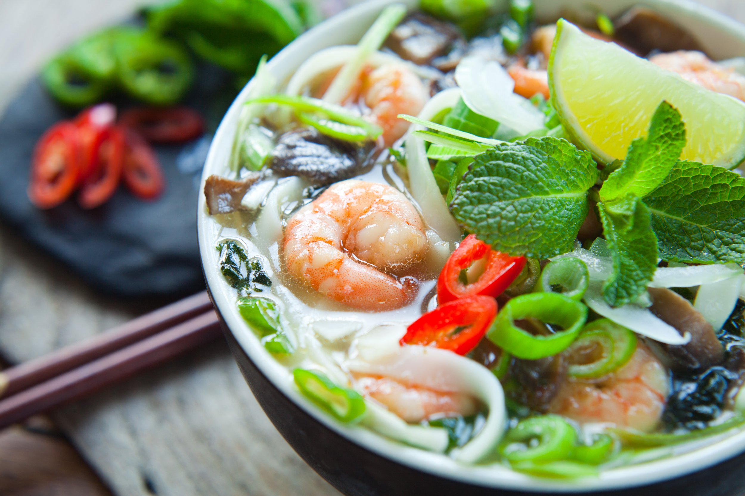 Bowl of fresh shrimp pho with greens, lime, and peppers