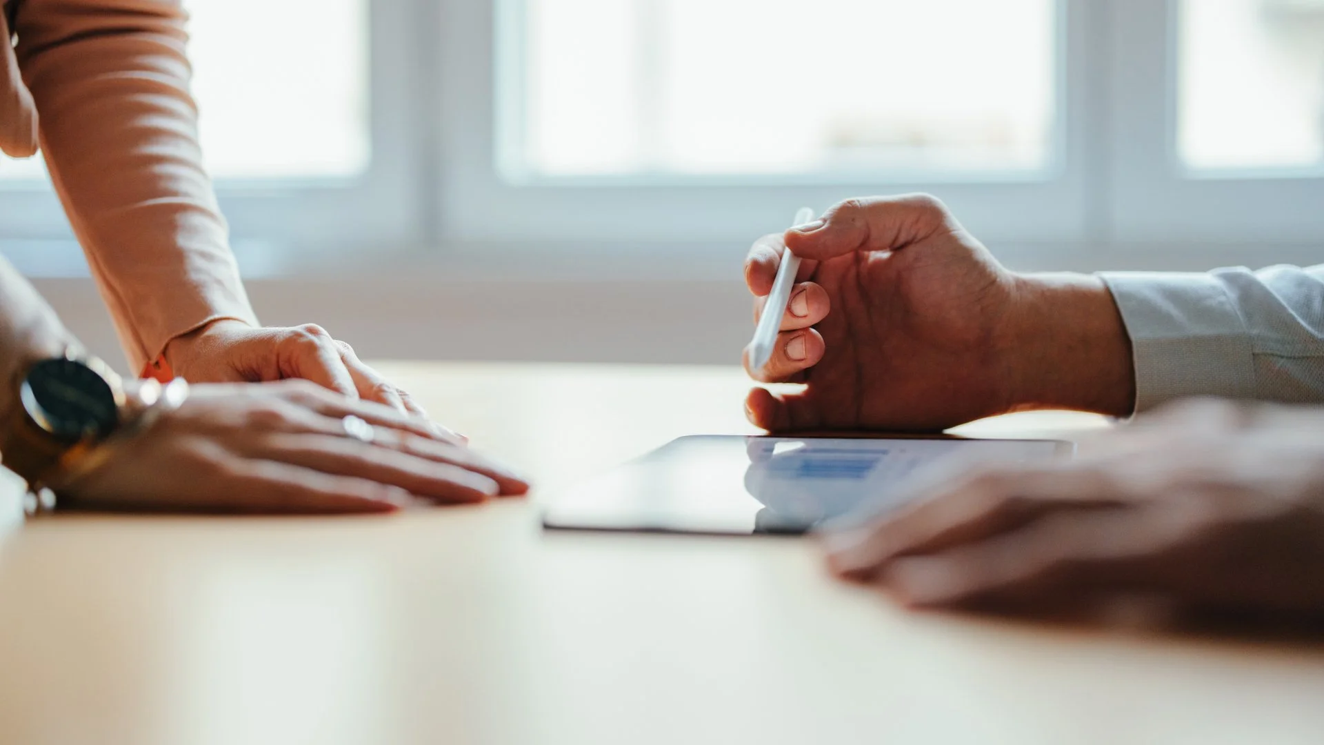 Two people conducting a business meeting or consultation at a desk, with formal attire and a digital tablet.