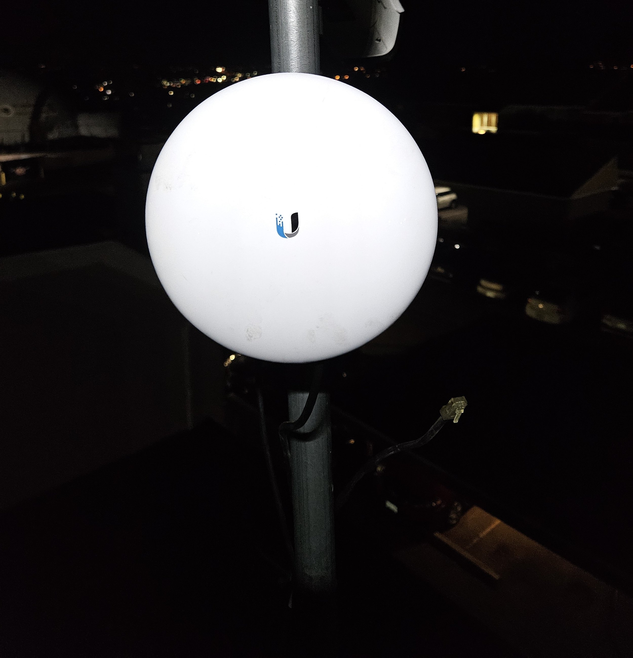 A spherical outdoor light fixture mounted on a pole at night with distant city lights in the background.