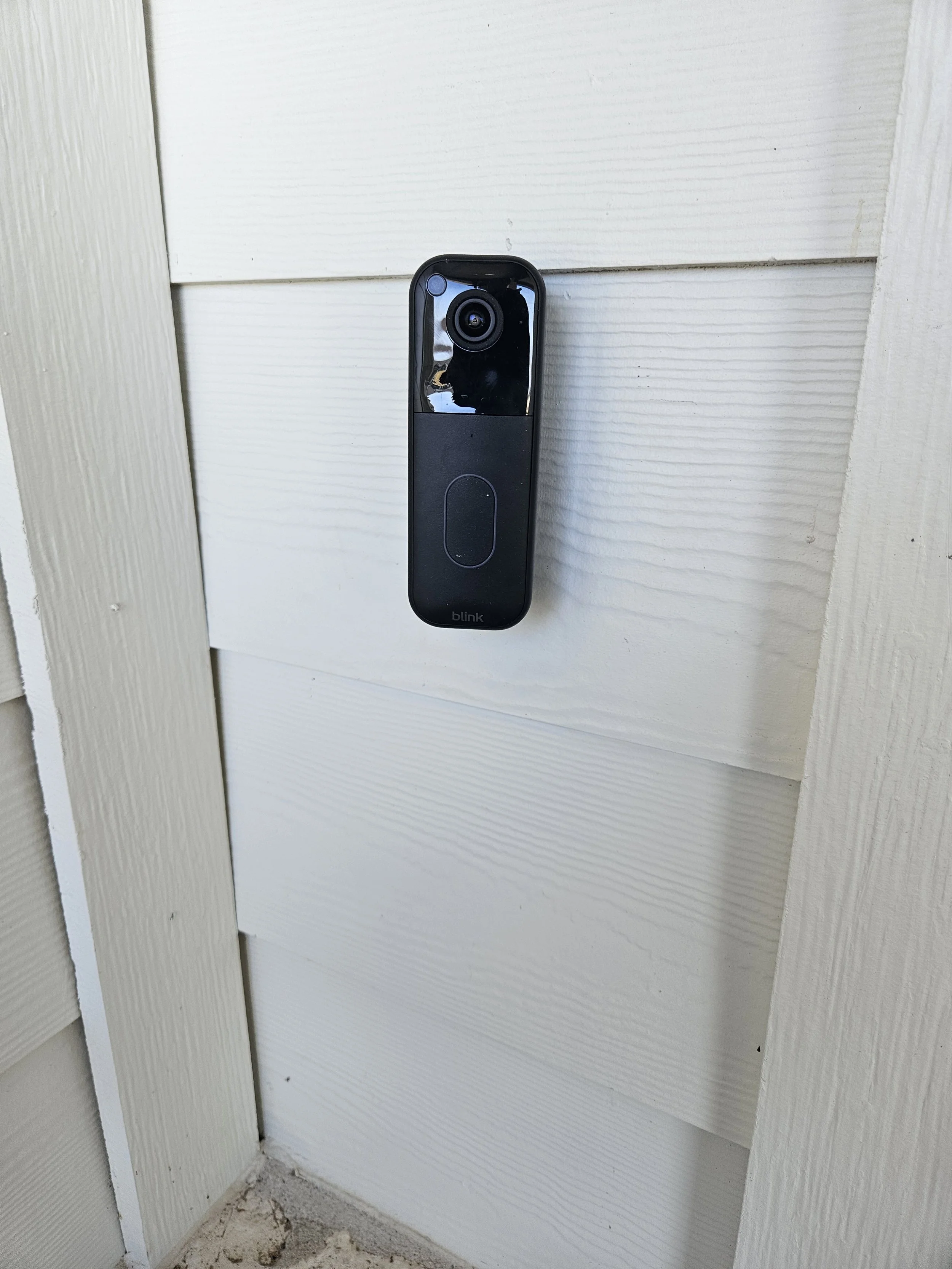 Video doorbell mounted on a white wooden exterior wall.
