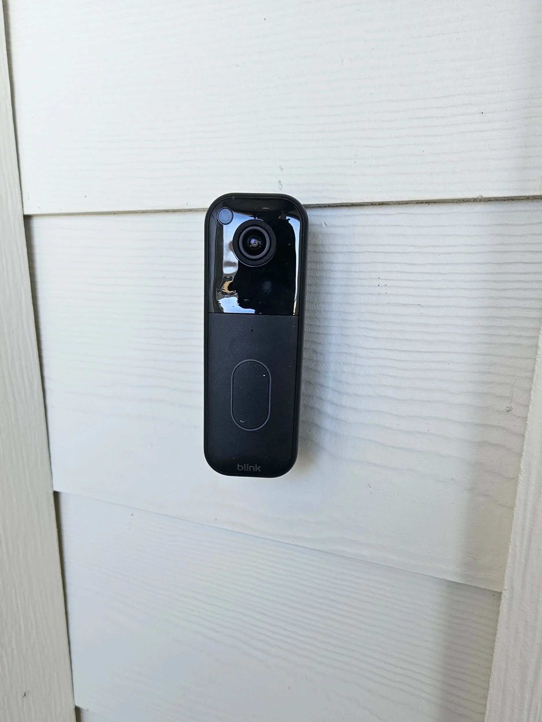 Video doorbell mounted on a white wooden exterior wall.