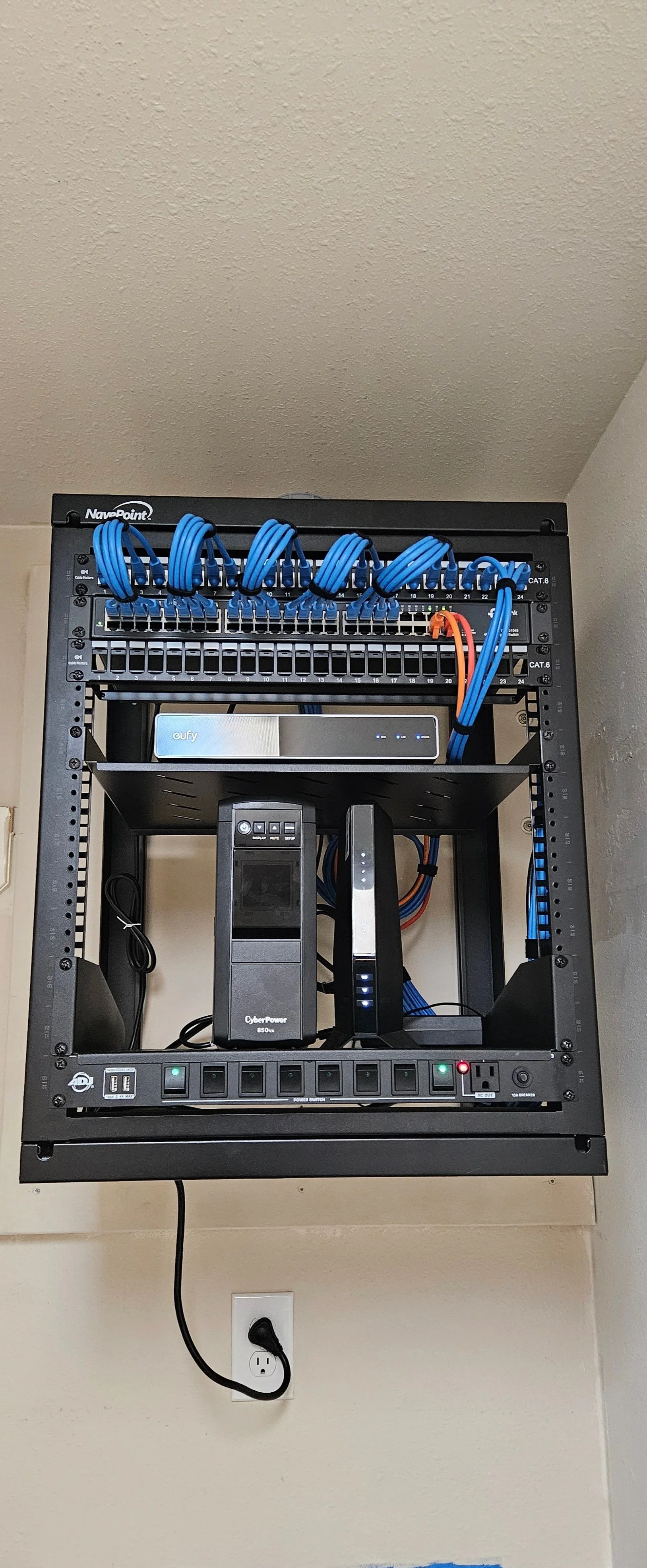Wall-mounted network and security rack with organized Cat6 patching, network switching, NVR, UPS backup, and power distribution.