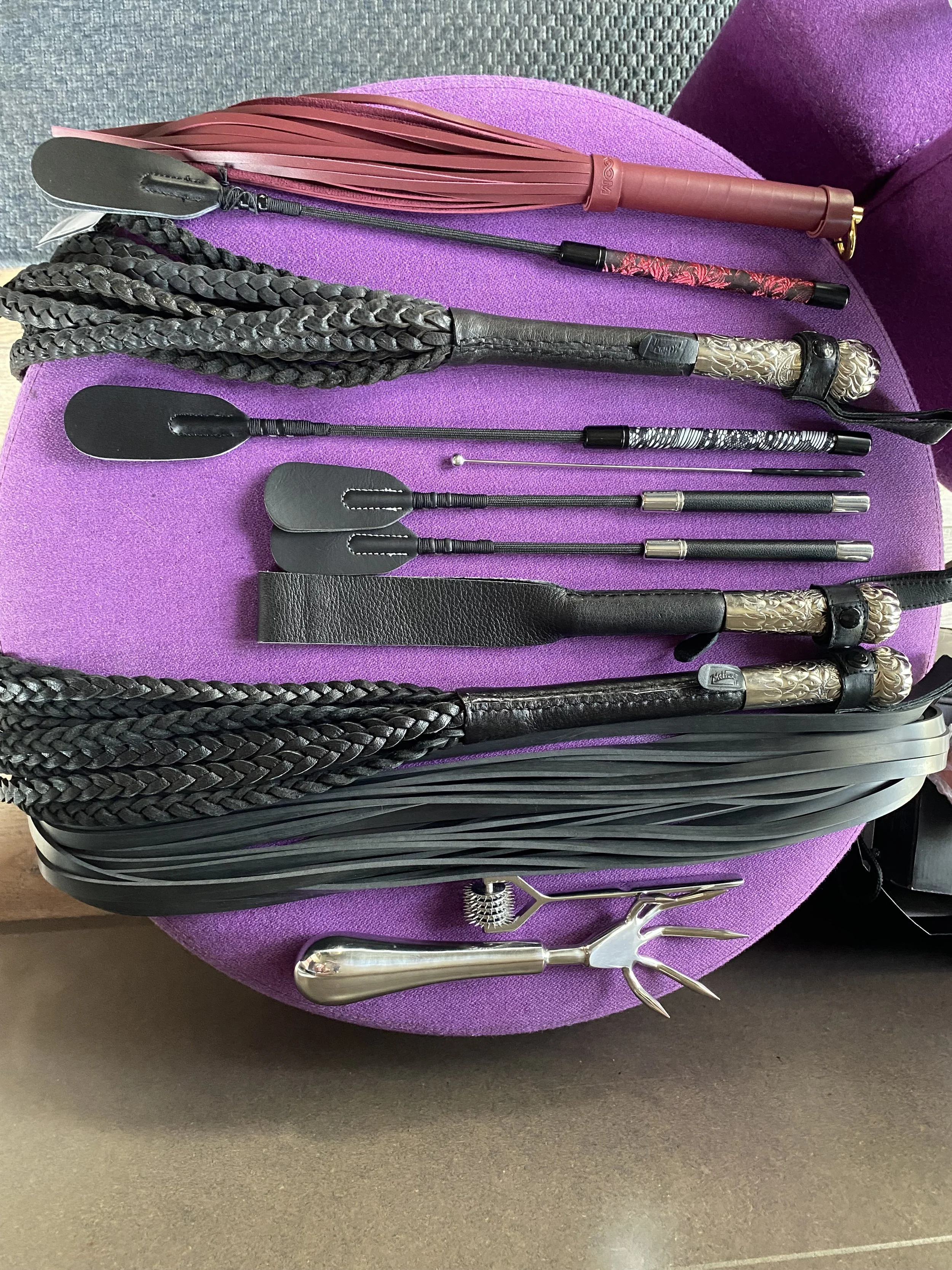 A collection of barbecue grilling tools, including tongs, spatulas, skewers, and a grill brush, all arranged on a purple chair.