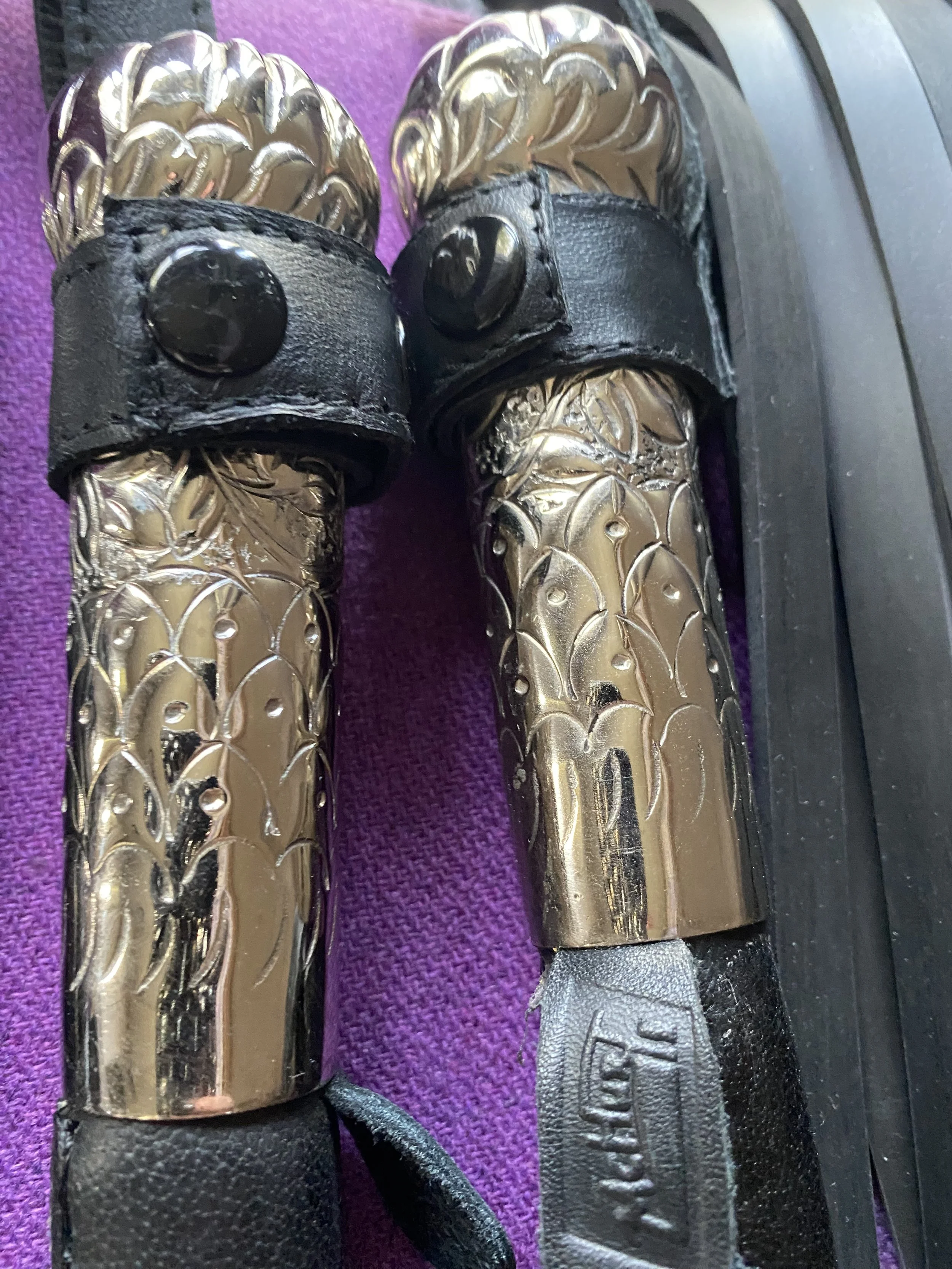 A pair of golf club grips with metallic gold dragon scale design and black strap with button, placed on a purple surface.