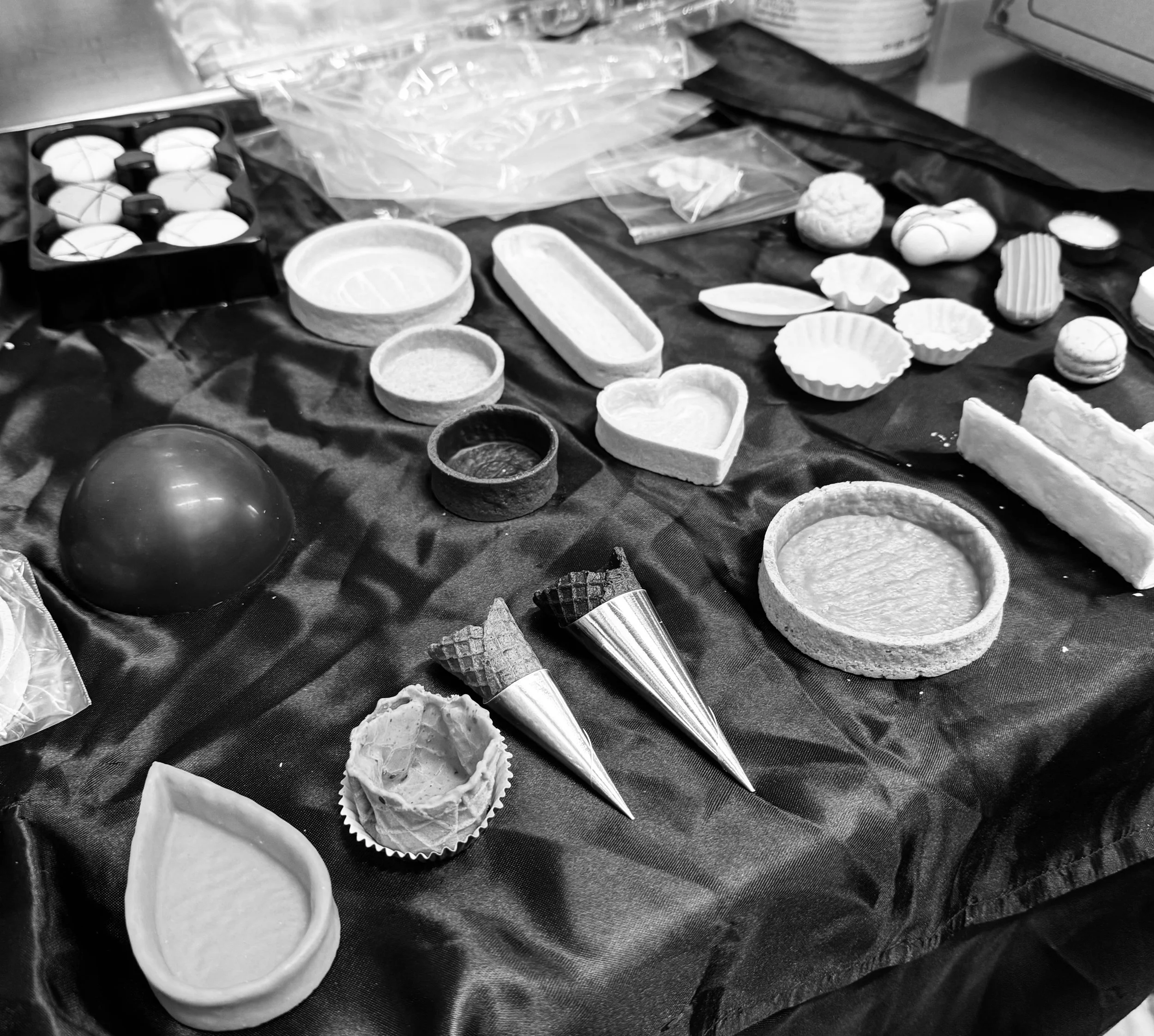 Various molds, cones, and tools for making rolled ice cream or similar desserts, arranged on a black tablecloth.