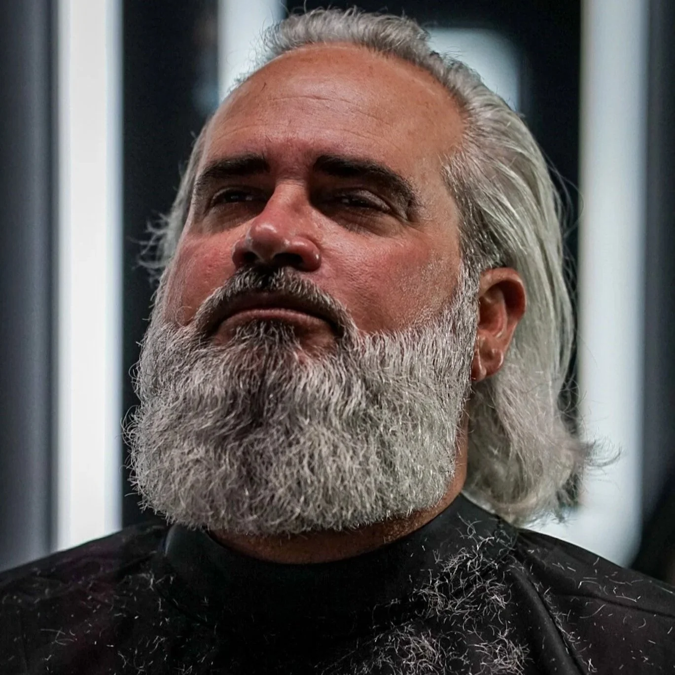 Close-up of a man with long gray hair and a thick gray beard, looking serious and contemplative.