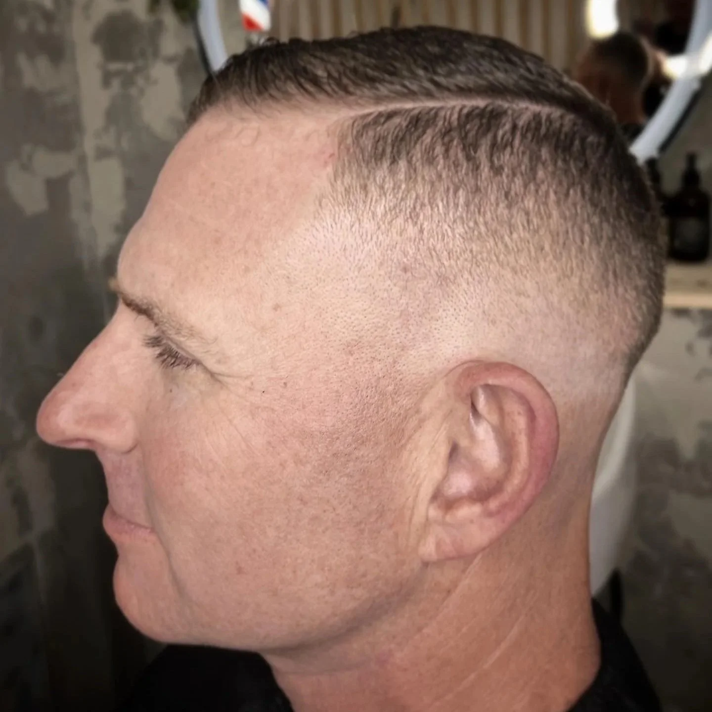 Close-up of a man's side profile with freshly cut short hair, high fade hairstyle, and clean shaven face, in a barbershop.