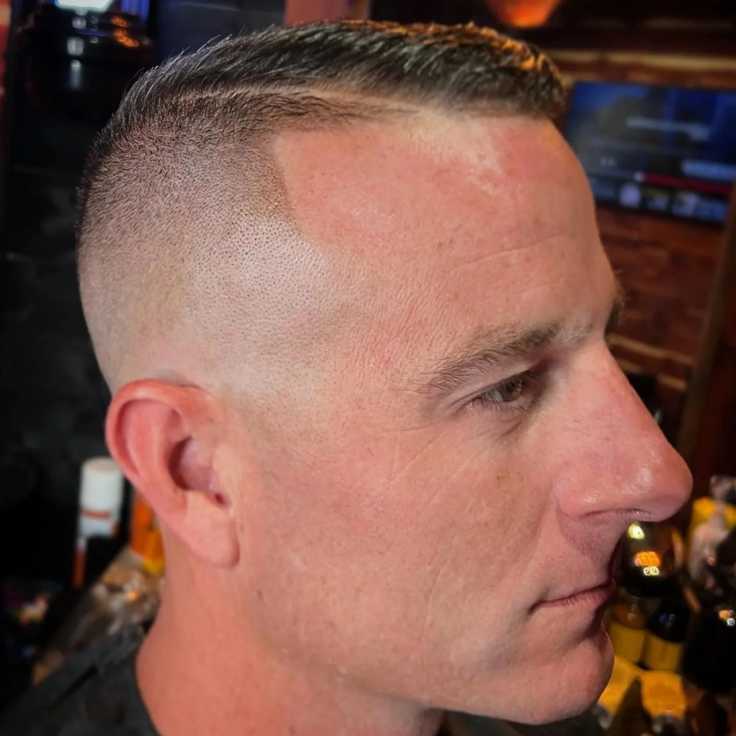 Close-up side profile of a man's fresh haircut with a faded sides and a combed-back top in a barbershop.