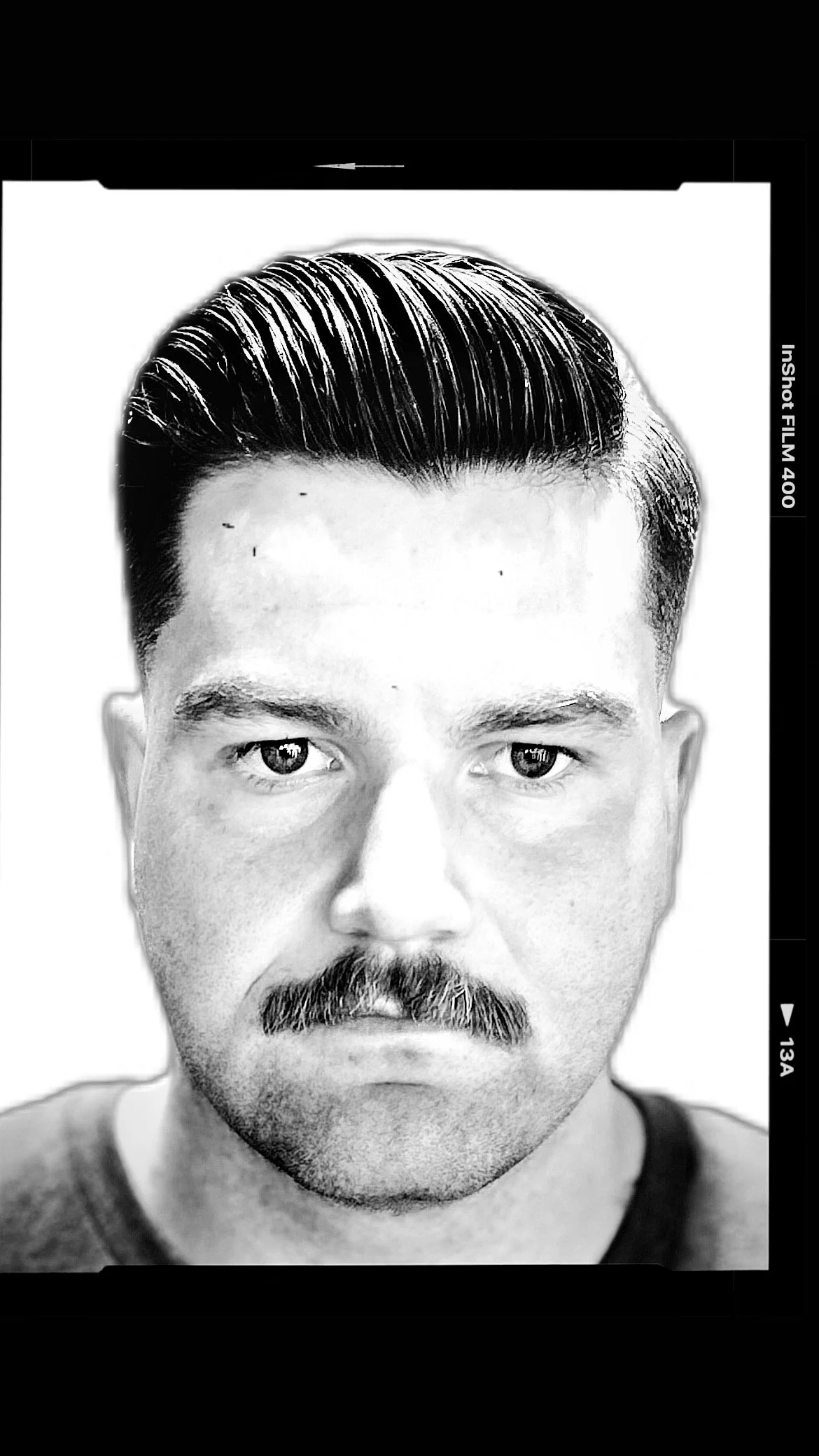 Black and white portrait of a man with a mustache and slicked-back hair, looking directly at the camera.