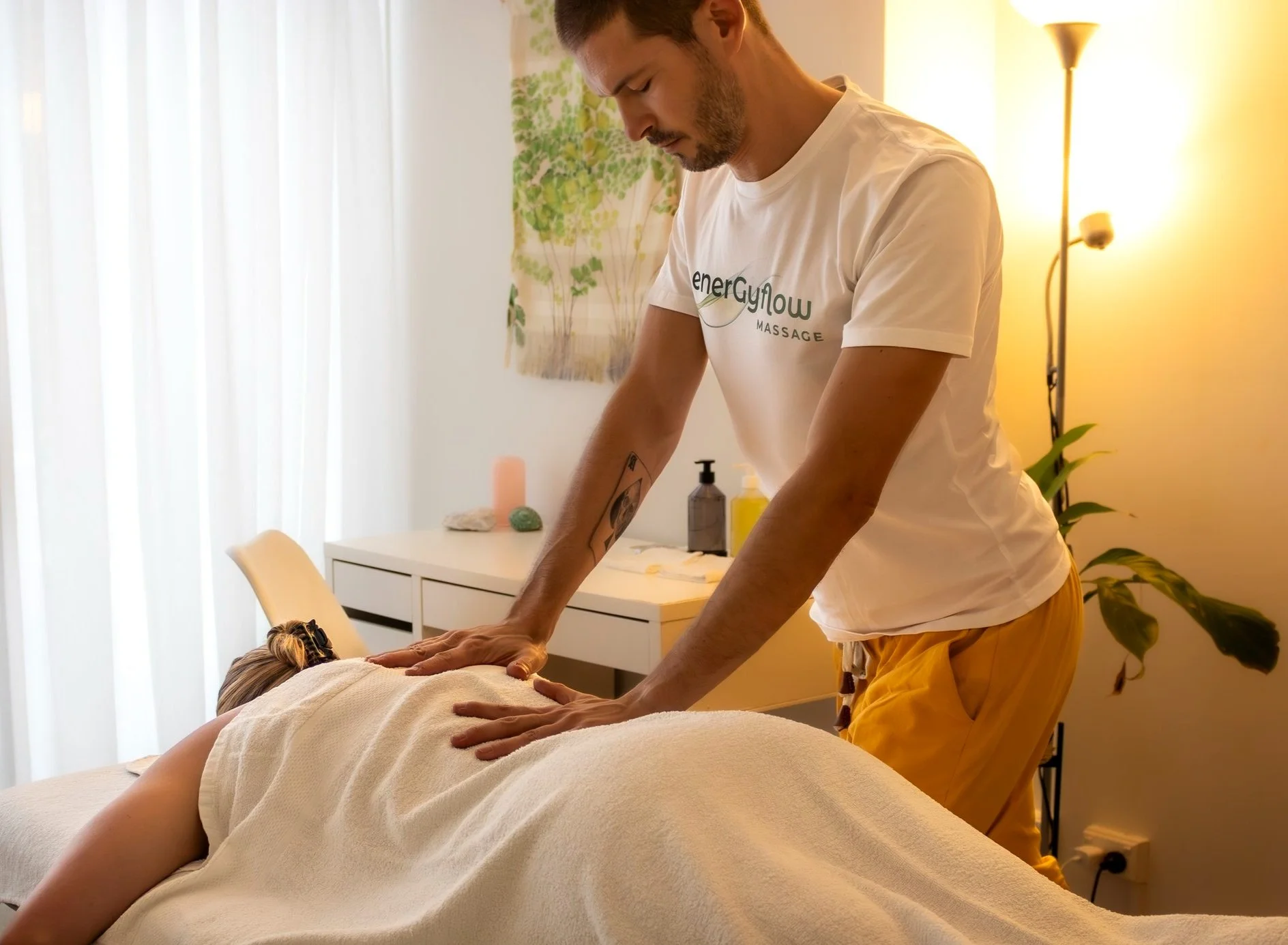 A massage therapist performing a back massage on a client lying face down on a massage table in a soft-lit room.