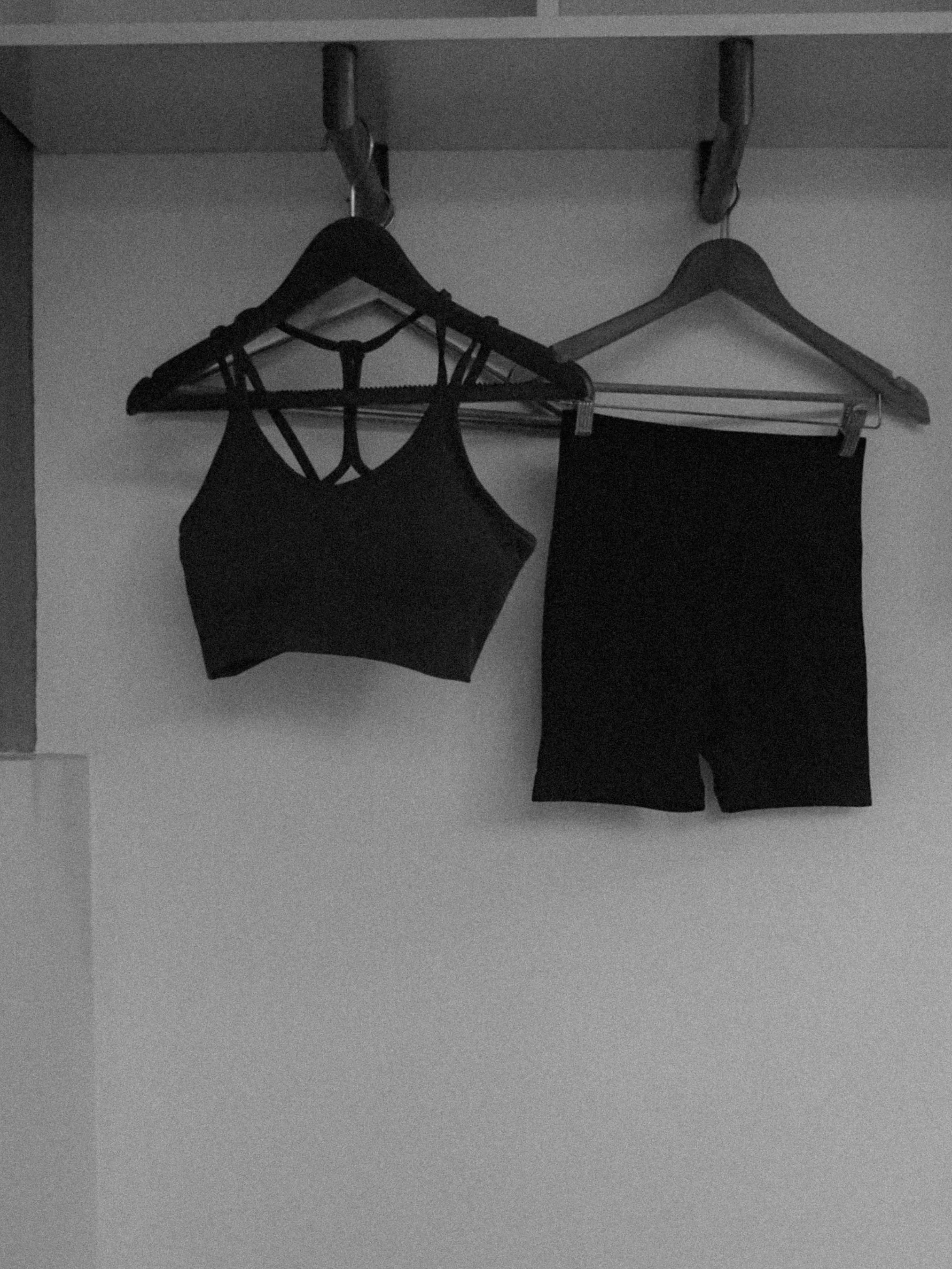 A black sports bra and black shorts hanging on wooden hangers inside a closet.