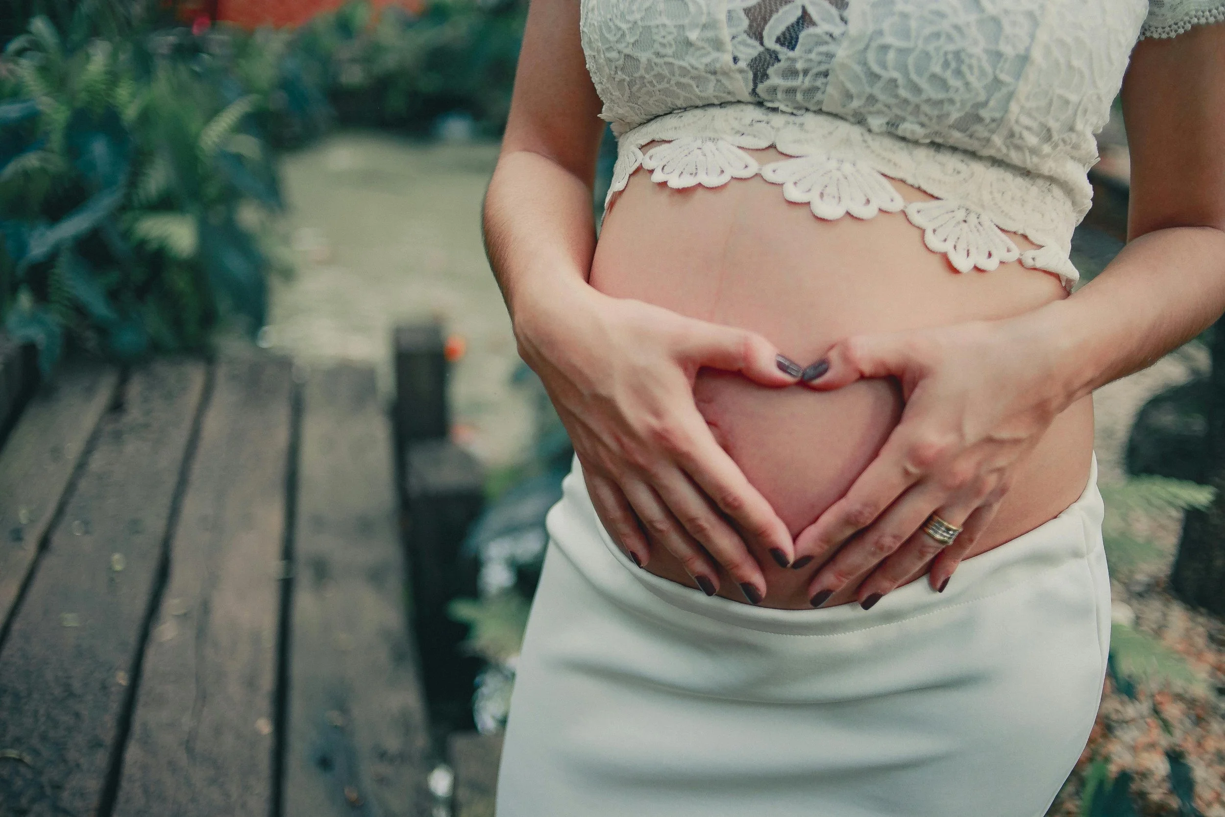 Pregnant woman gently shaping a heart with her hands over her belly, symbolizing fertility and pregnancy in an article comparing IVF and natural conception success rates.