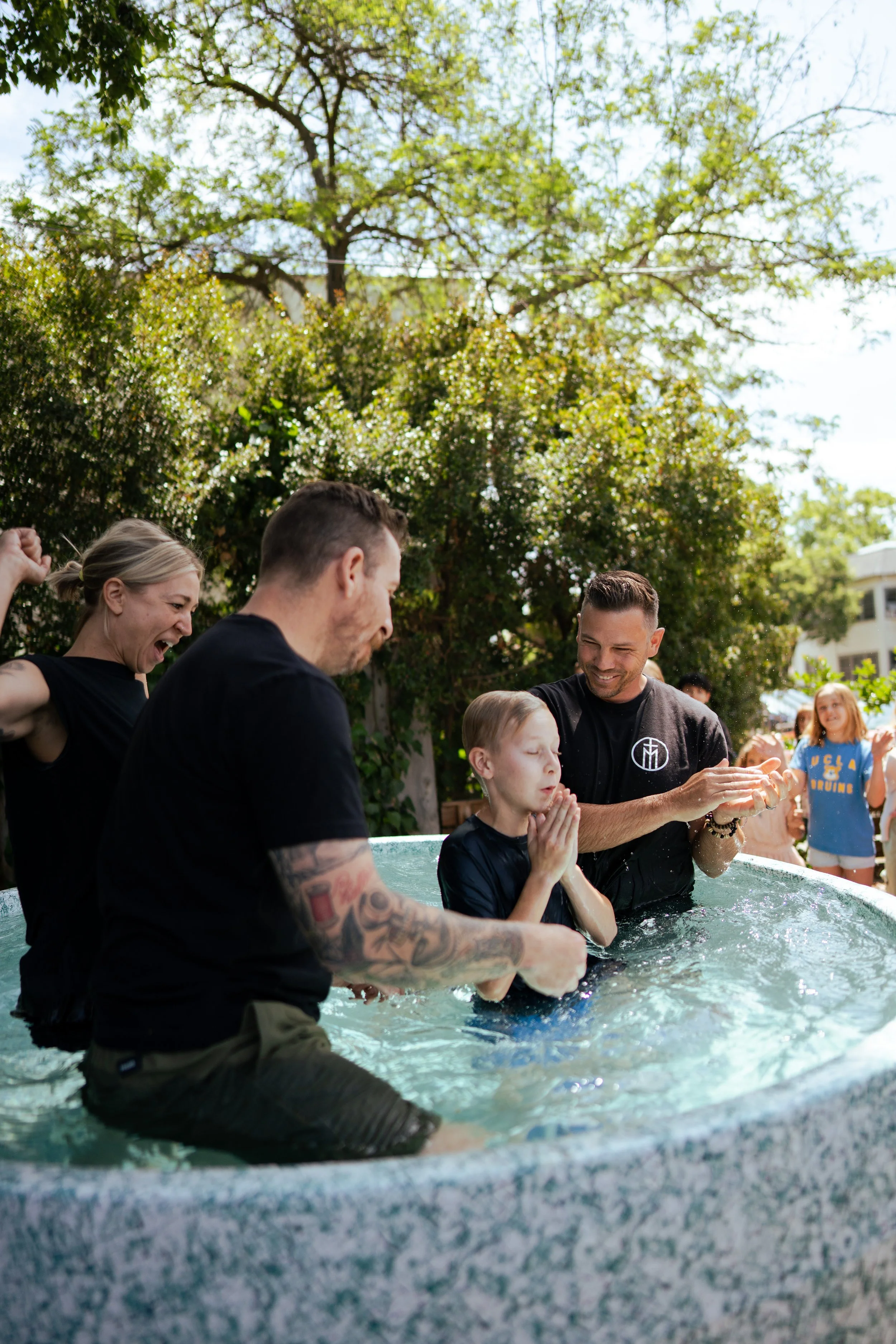 People participating in a baptism ceremony outdoors in a clear water baptismal pool.