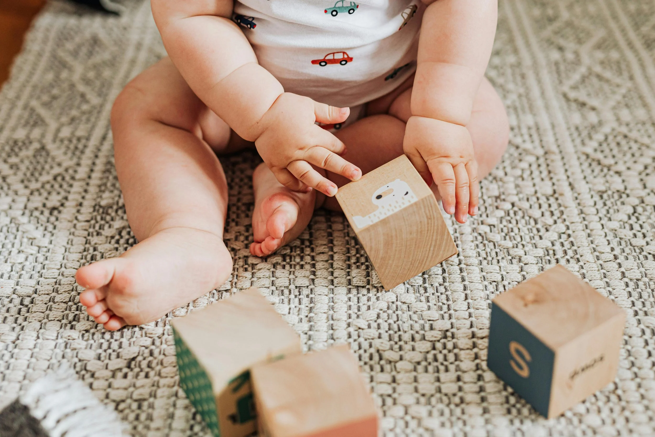 Baby playing with wooden blocks on a textured rug.