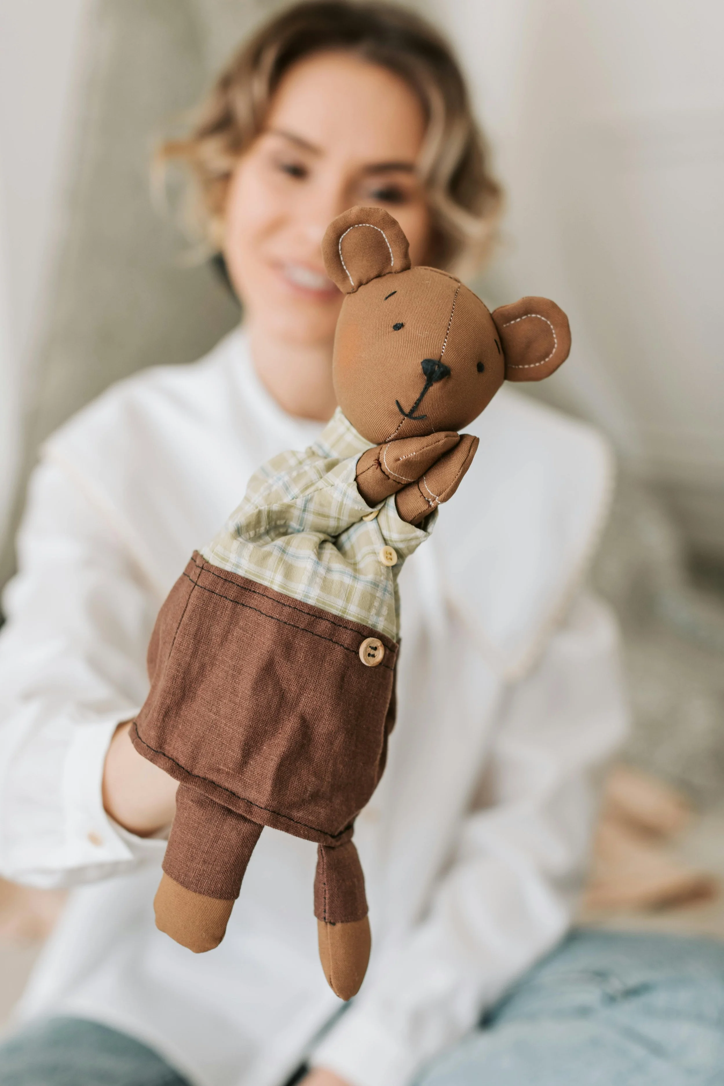 Person holding a brown bear hand puppet with a plaid shirt and brown pants.