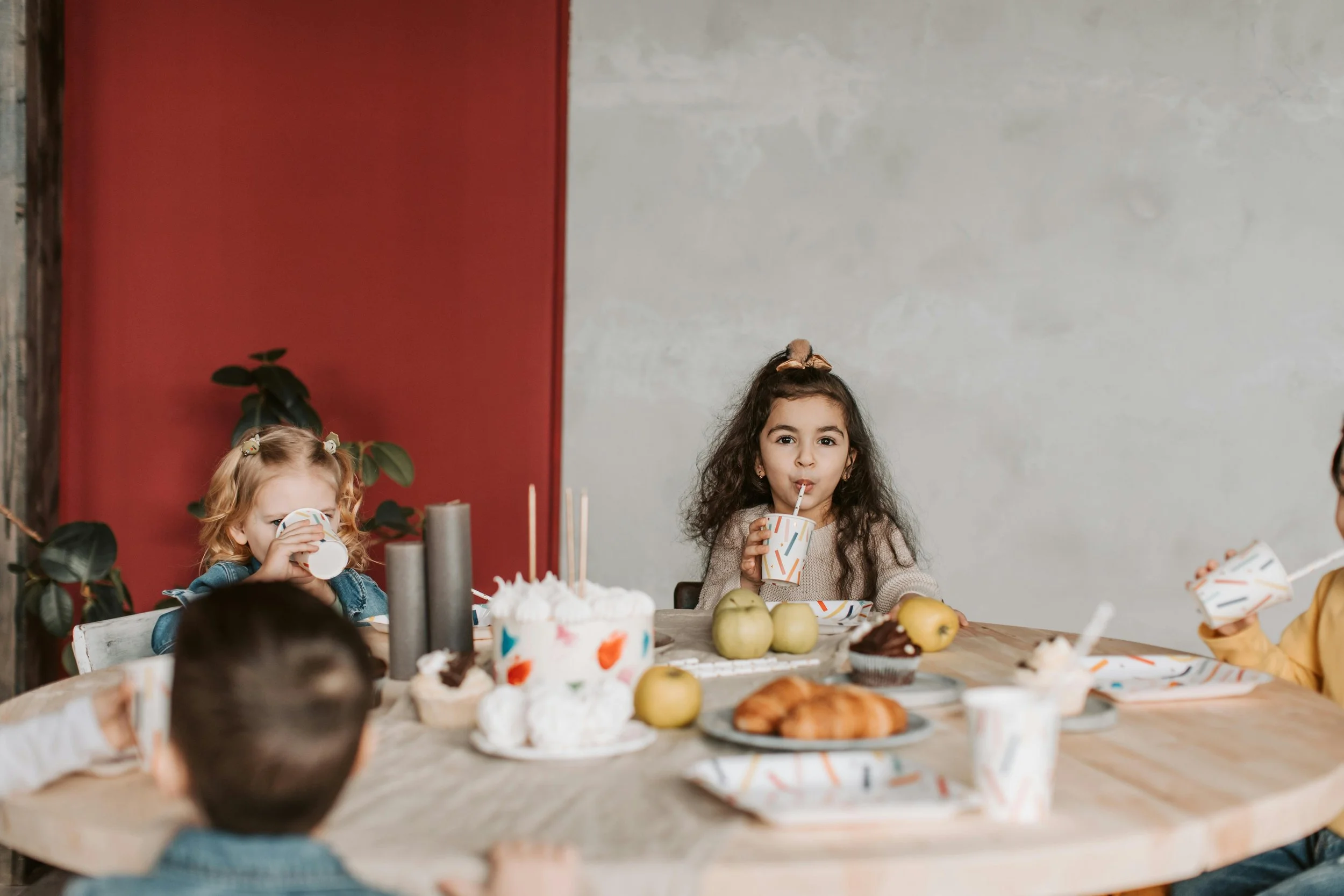 Children sitting at a table with desserts and fruits during a party.