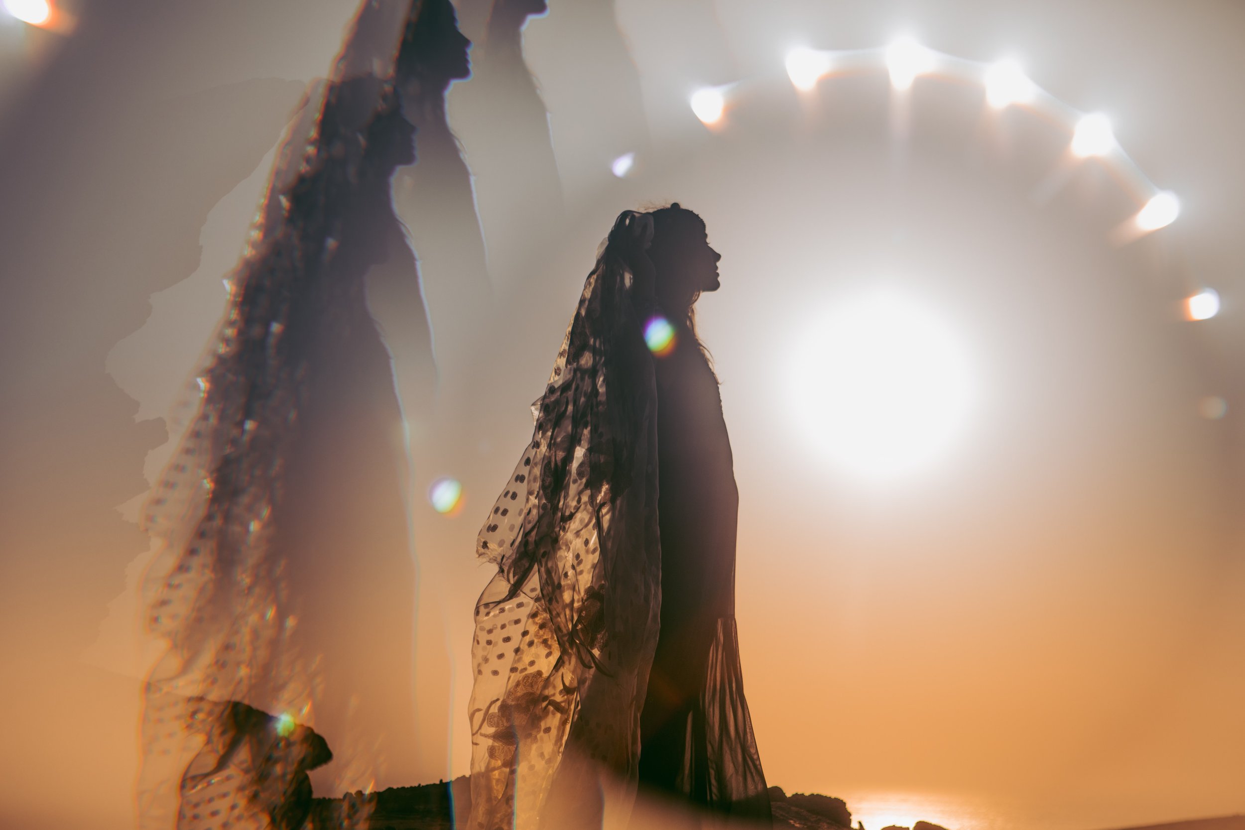 Silhouettes of a woman wearing a veil against a sunset with a large bright sun and a circular structure with lights