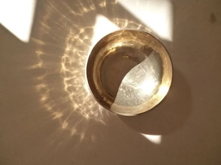 A shiny metallic bowl reflecting sunlight, creating a pattern of light and shadow on a light-colored surface.